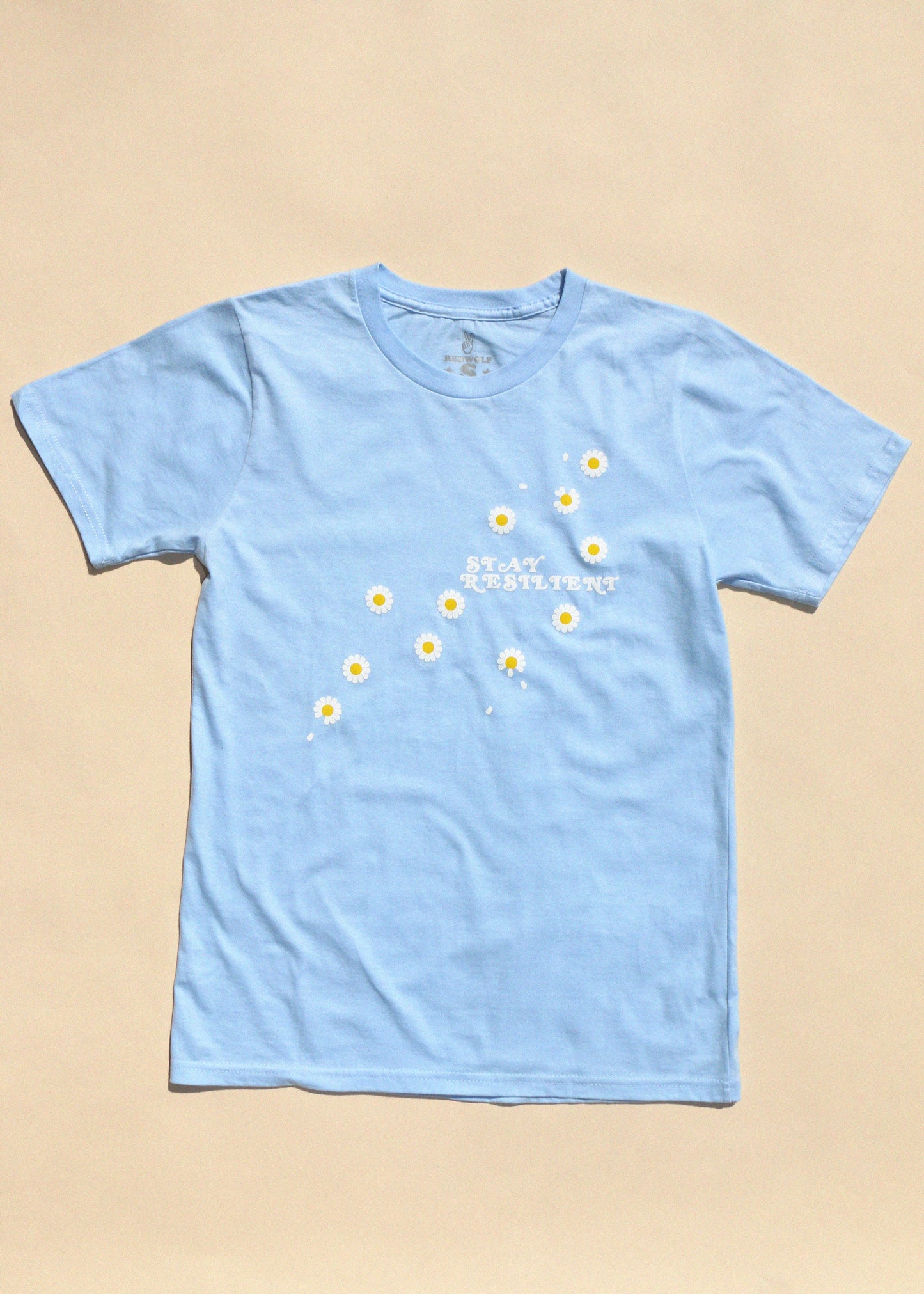 Light blue t-shirt with white text and yellow daisy graphics on a beige background