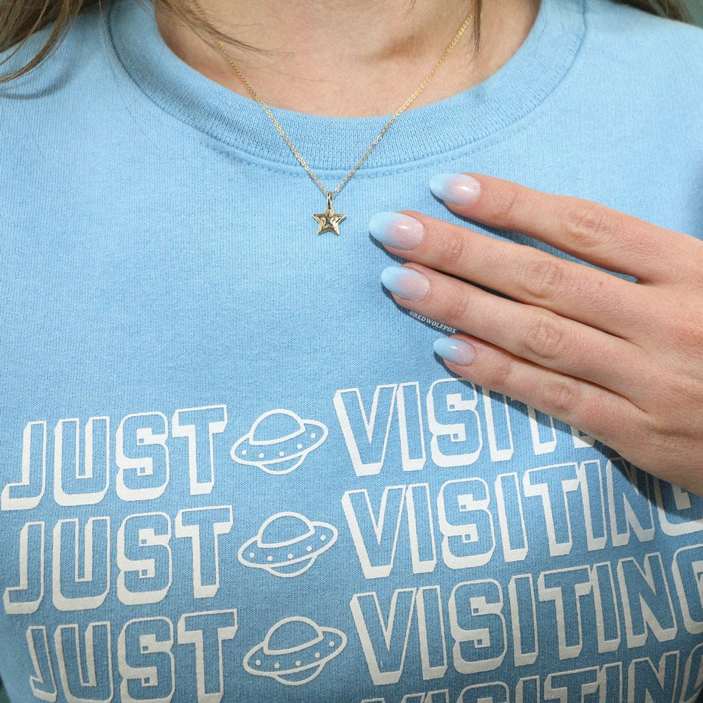 Brass 3-d layered starburst charm hanging from brass chain being worn against a baby blue crewneck sweatshirt