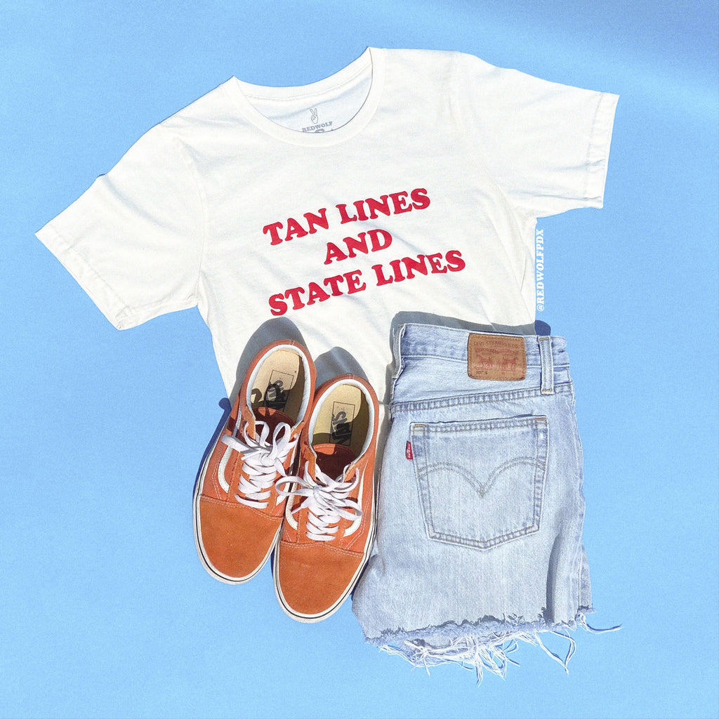 'TAN LINES AND STATE LINES' text graphic on white tee paired with orange sneakers and denim shorts against light blue backdrop