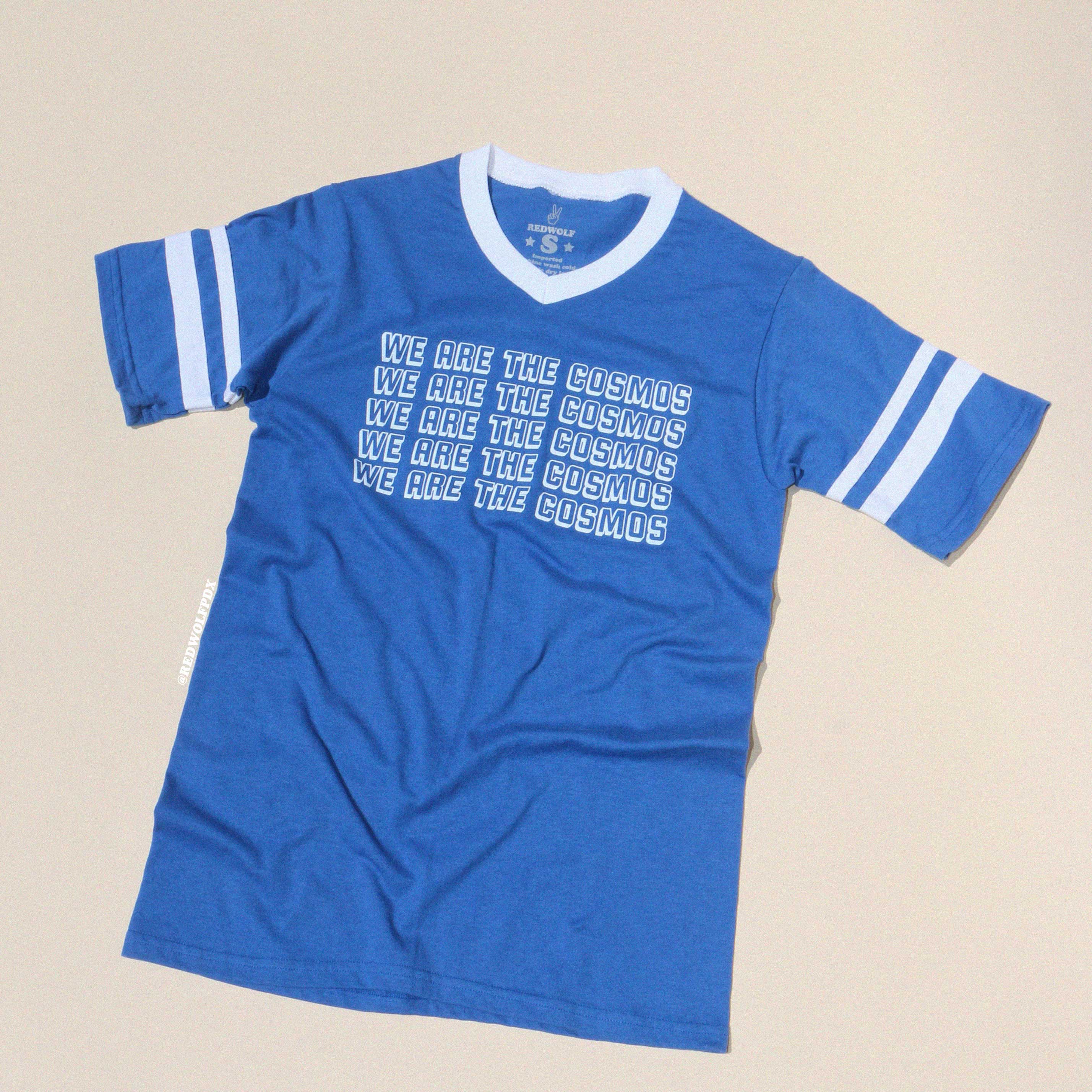 Blue t-shirt with 'We Are The Cosmos' text on a beige background
