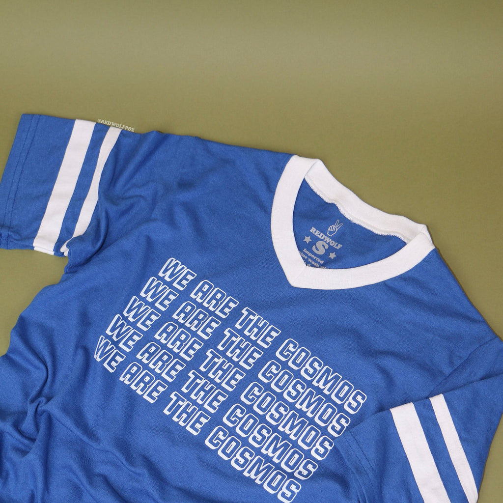 Blue t-shirt with 'We Are The Cosmos' text on a vintage green backdrop
