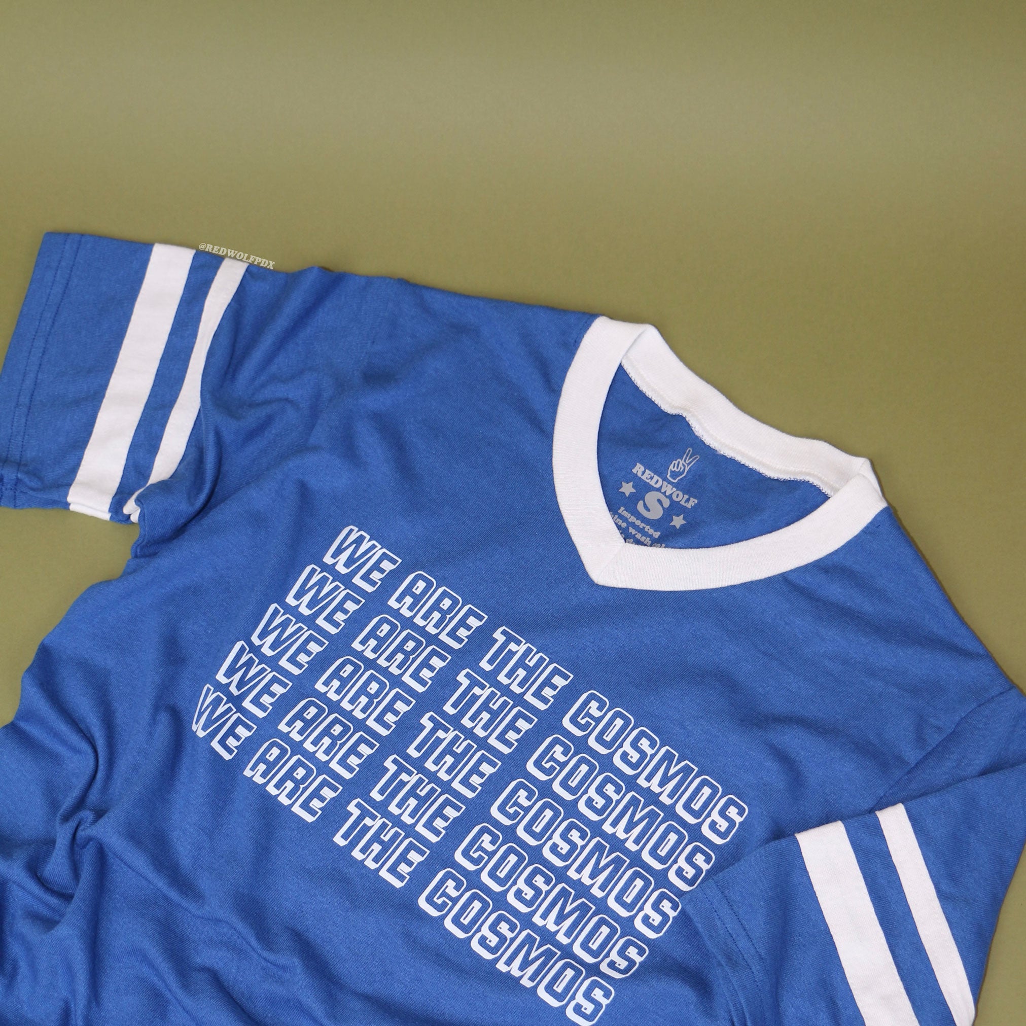 Blue t-shirt with 'We Are The Cosmos' text on a vintage green backdrop