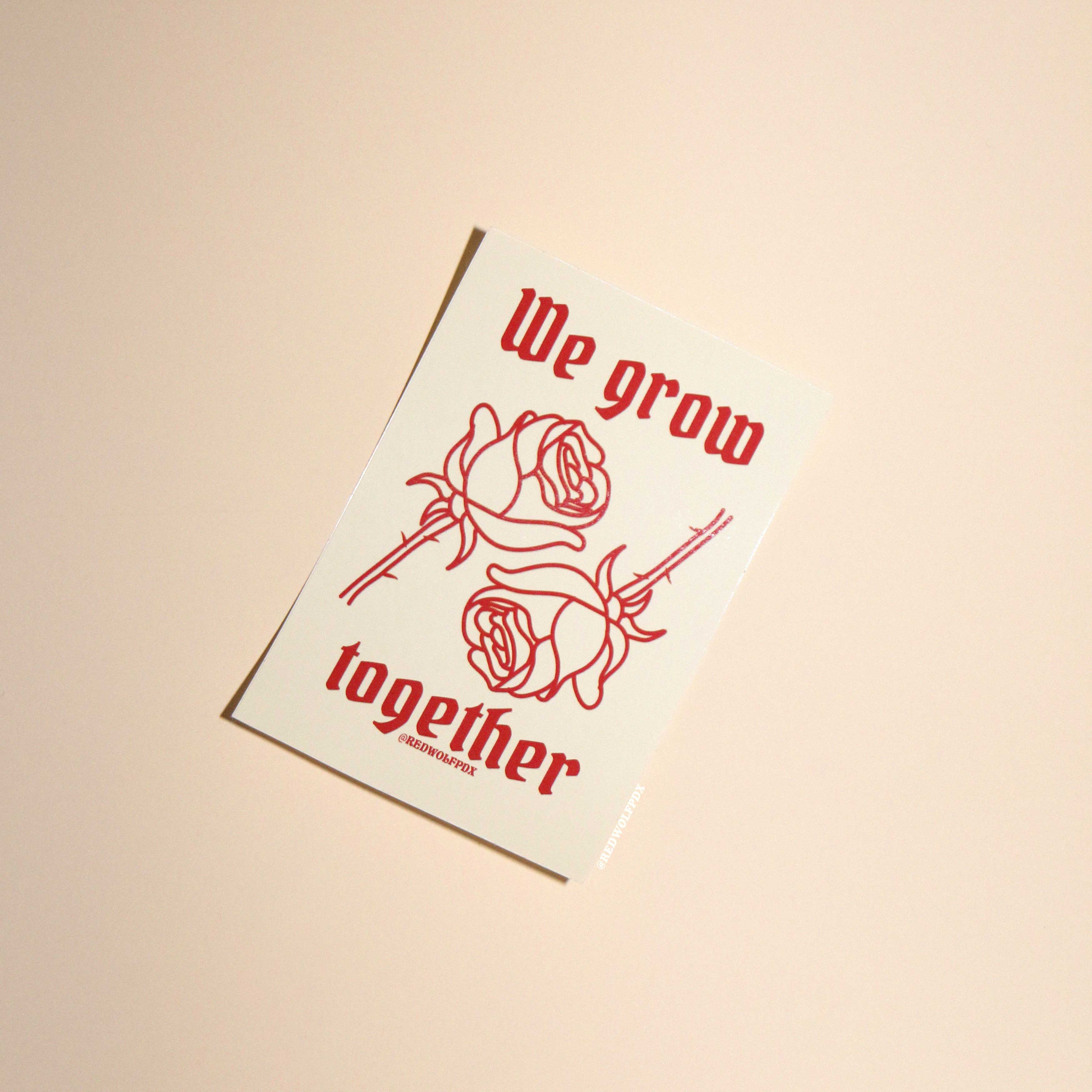beige sticker with text 'We grow together  in gothic font with 2 red roses illustration graphic sticker on beige 
backdrop