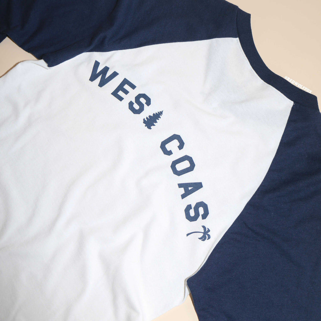 A navy blue and white raglan shirt with the text 'WEST COAST' printed across the back