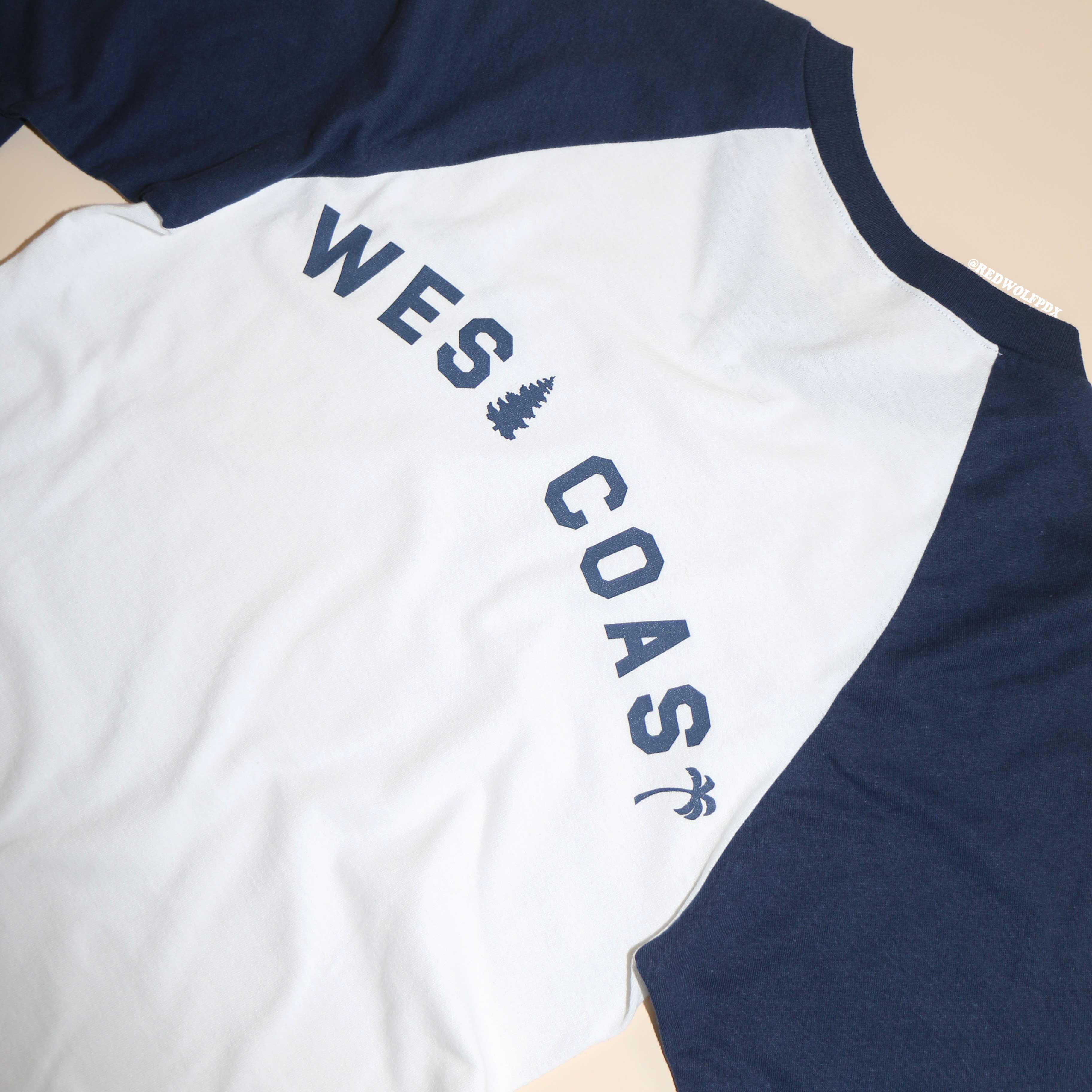 A navy blue and white raglan shirt with the text 'WEST COAST' printed across the back