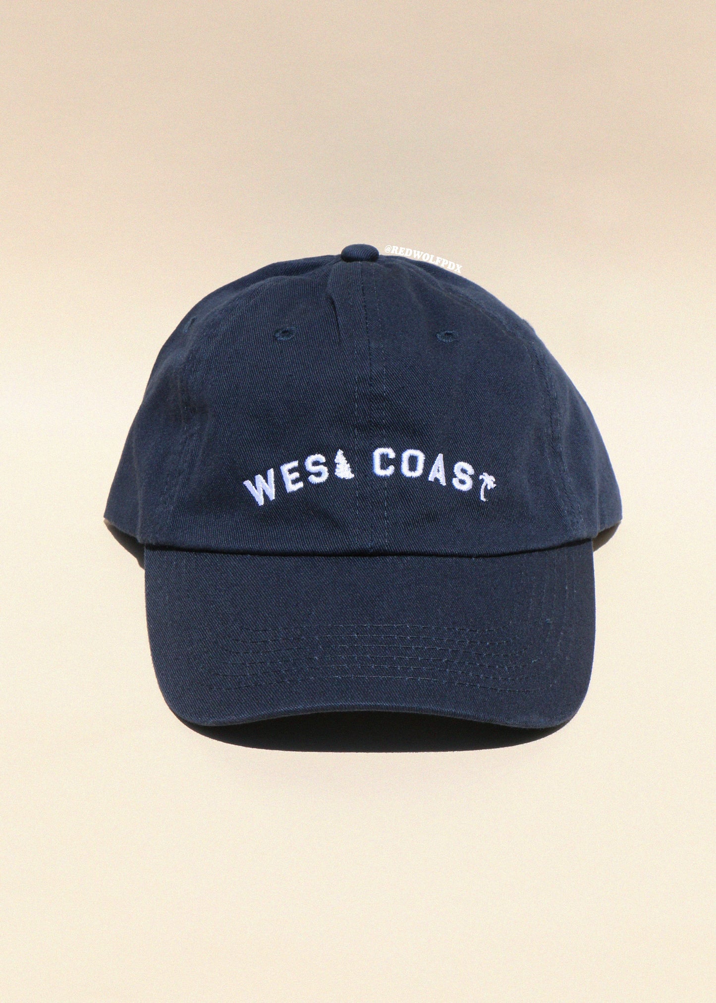 Navy blue cap with 'West Coast' text on a beige background