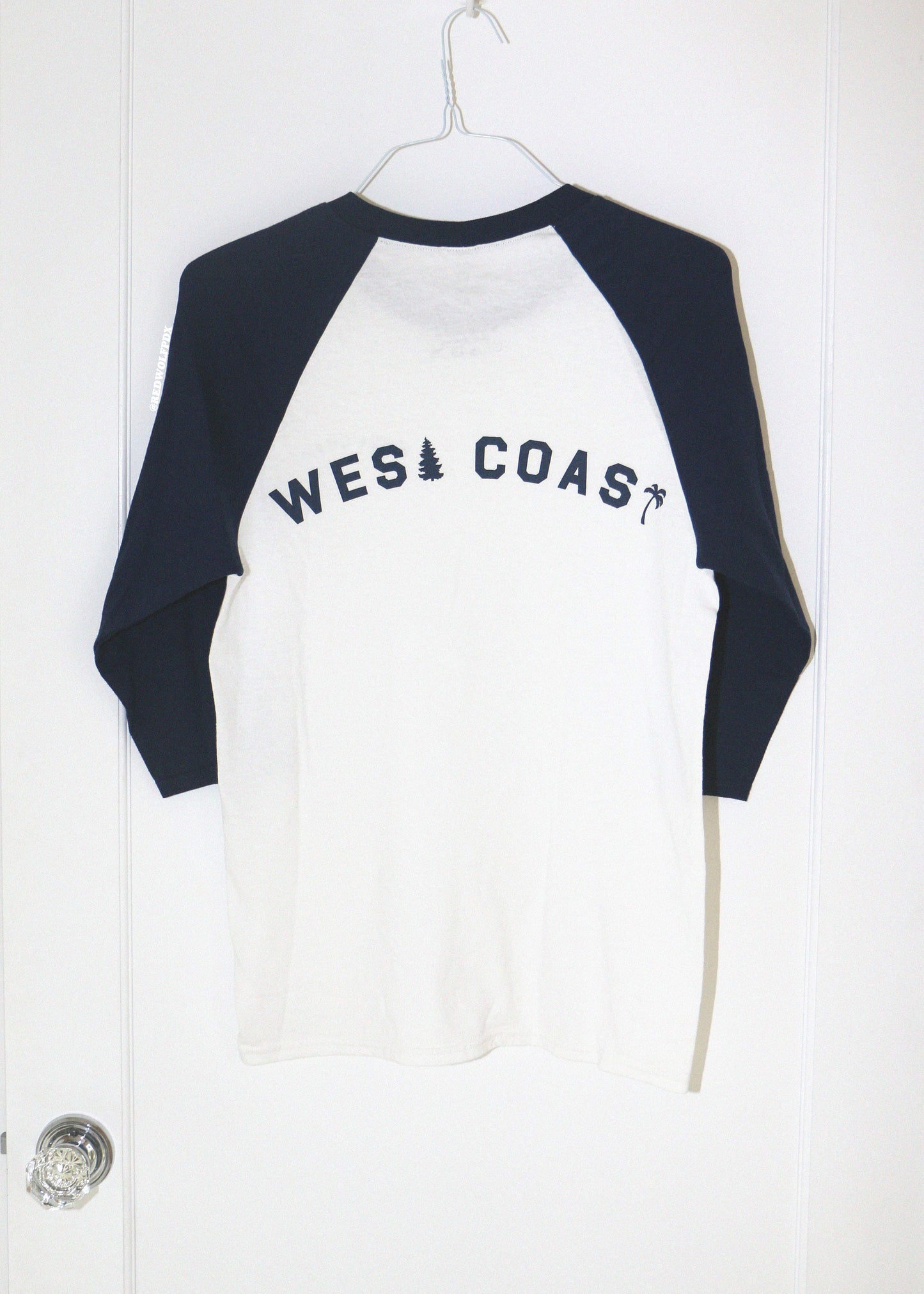 White and navy blue long-sleeve shirt with 'West Coast' text on a white door background