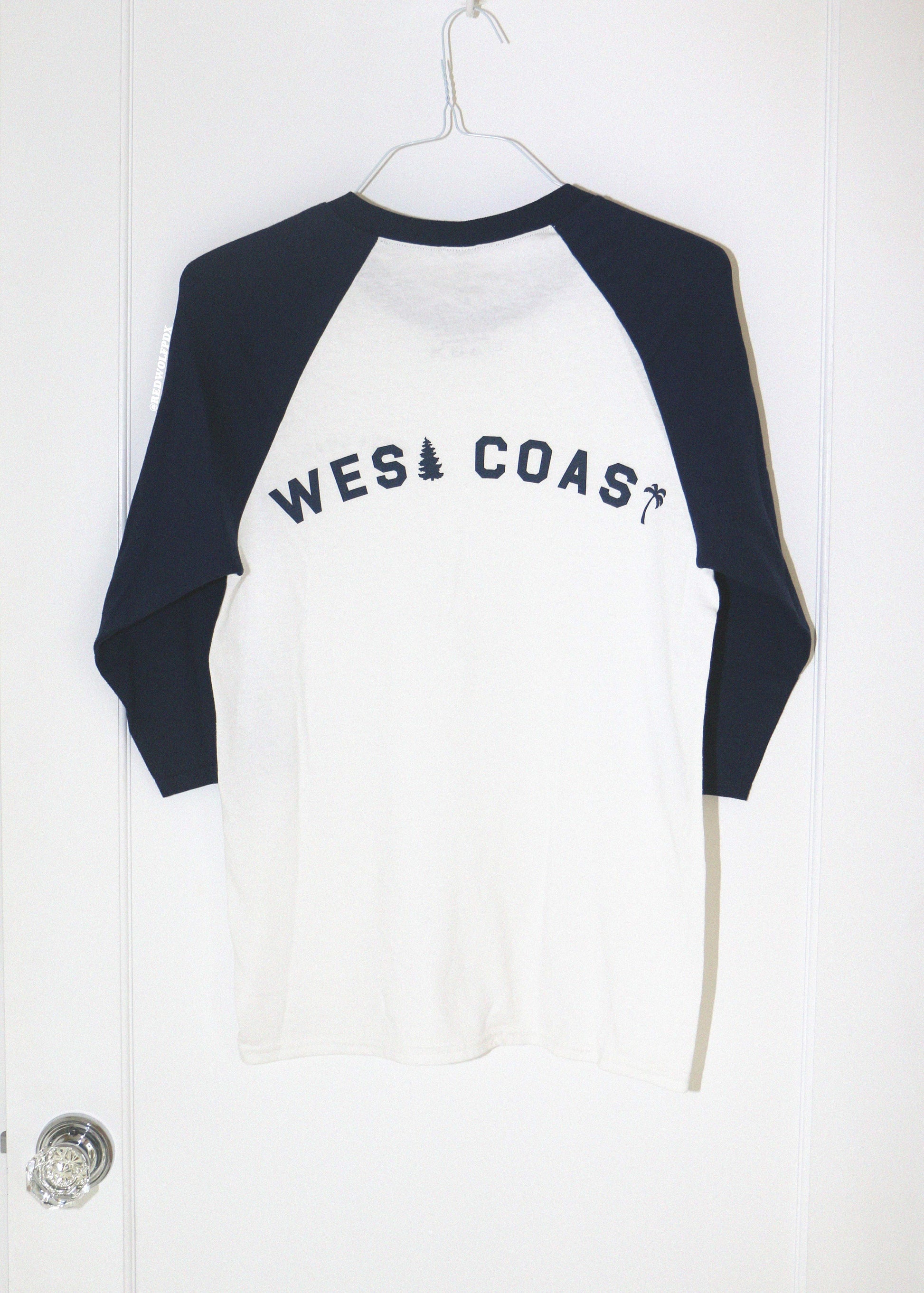 White and navy blue long-sleeve shirt with 'West Coast' text on a white door background