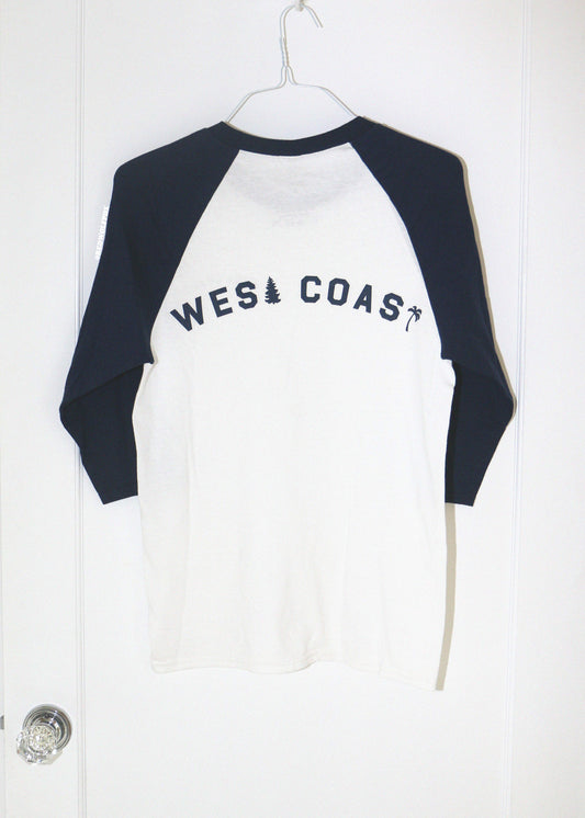 White and navy blue long-sleeve shirt with 'West Coast' text on a white door background