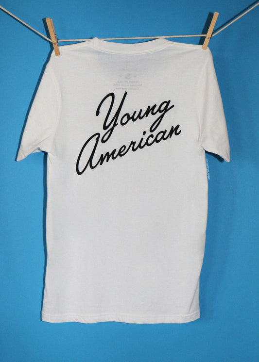 A white short-sleeve t-shirt hanging from a clothesline with wooden clothespins against a bright blue background. The back of the shirt features the words 'Young American' printed in a black cursive script.