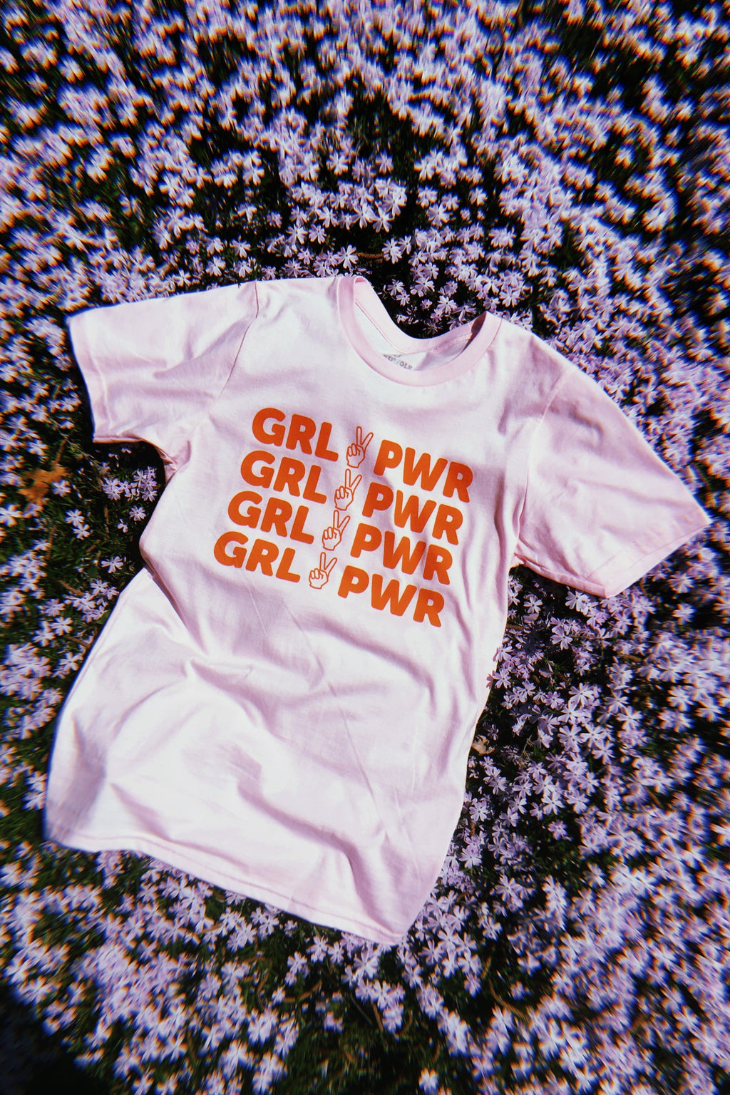 pink tee with text 'GRL PWR' and peace sign graphic in red/orange ink screen printed down the front on a bed of purple flowers 