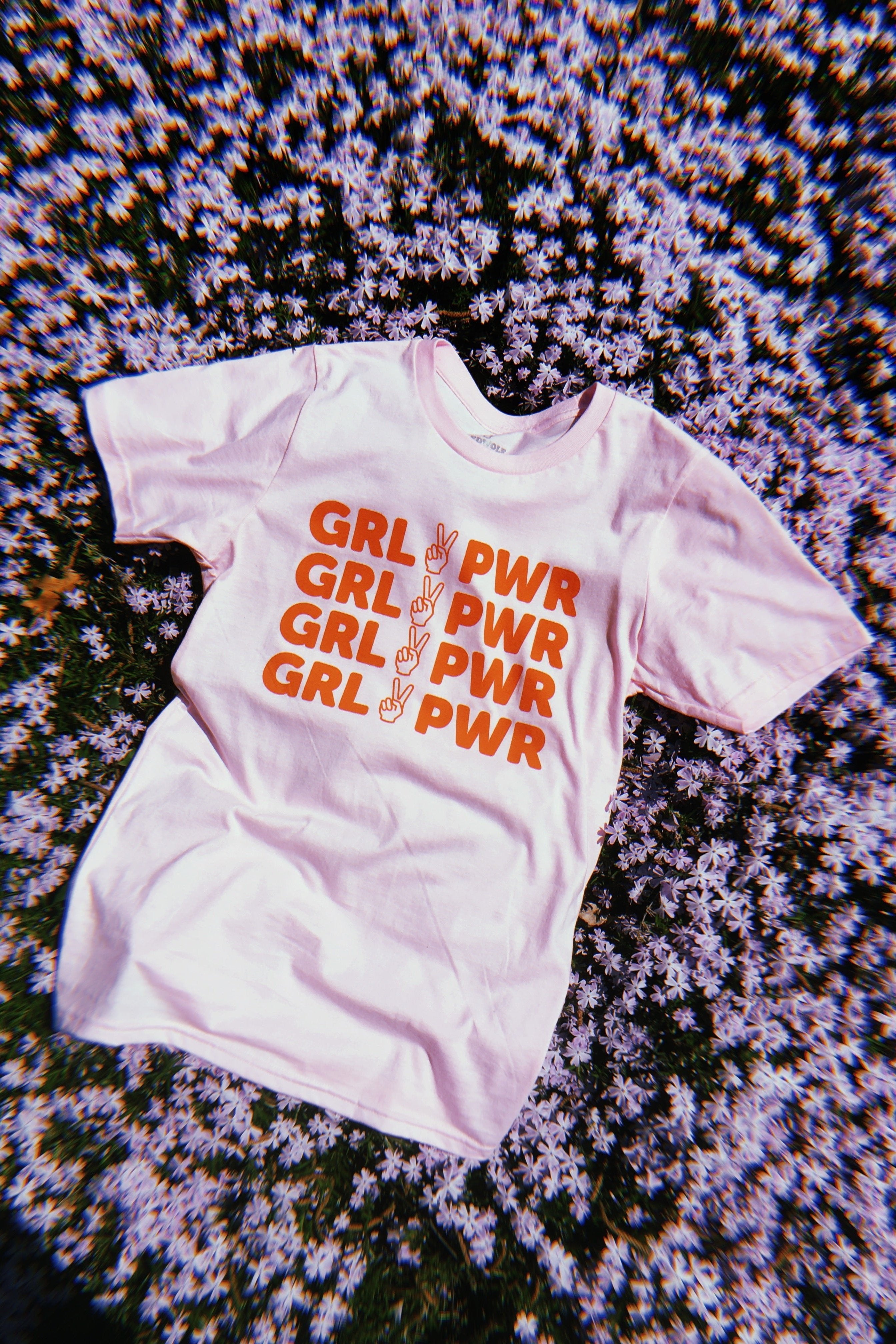 pink tee with text 'GRL PWR' and peace sign graphic in red/orange ink screen printed down the front on a bed of purple flowers 