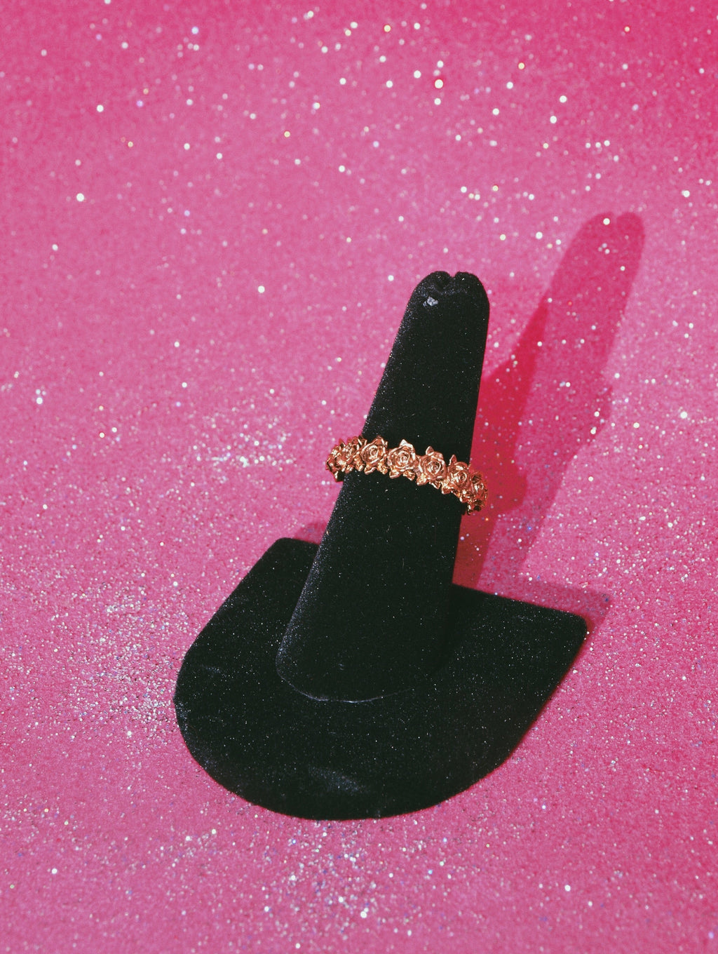 Brass rose wreath ring on black velvet ring stand against sparkly pink backdrop
