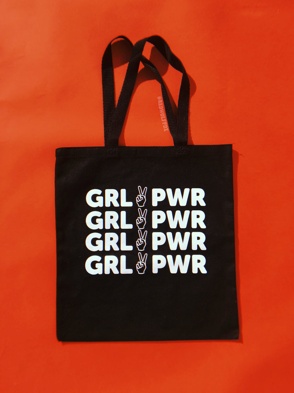 Black canvas tote bag with text 'GRL PWR' in white ink screen printed across on a vintage red backdrop