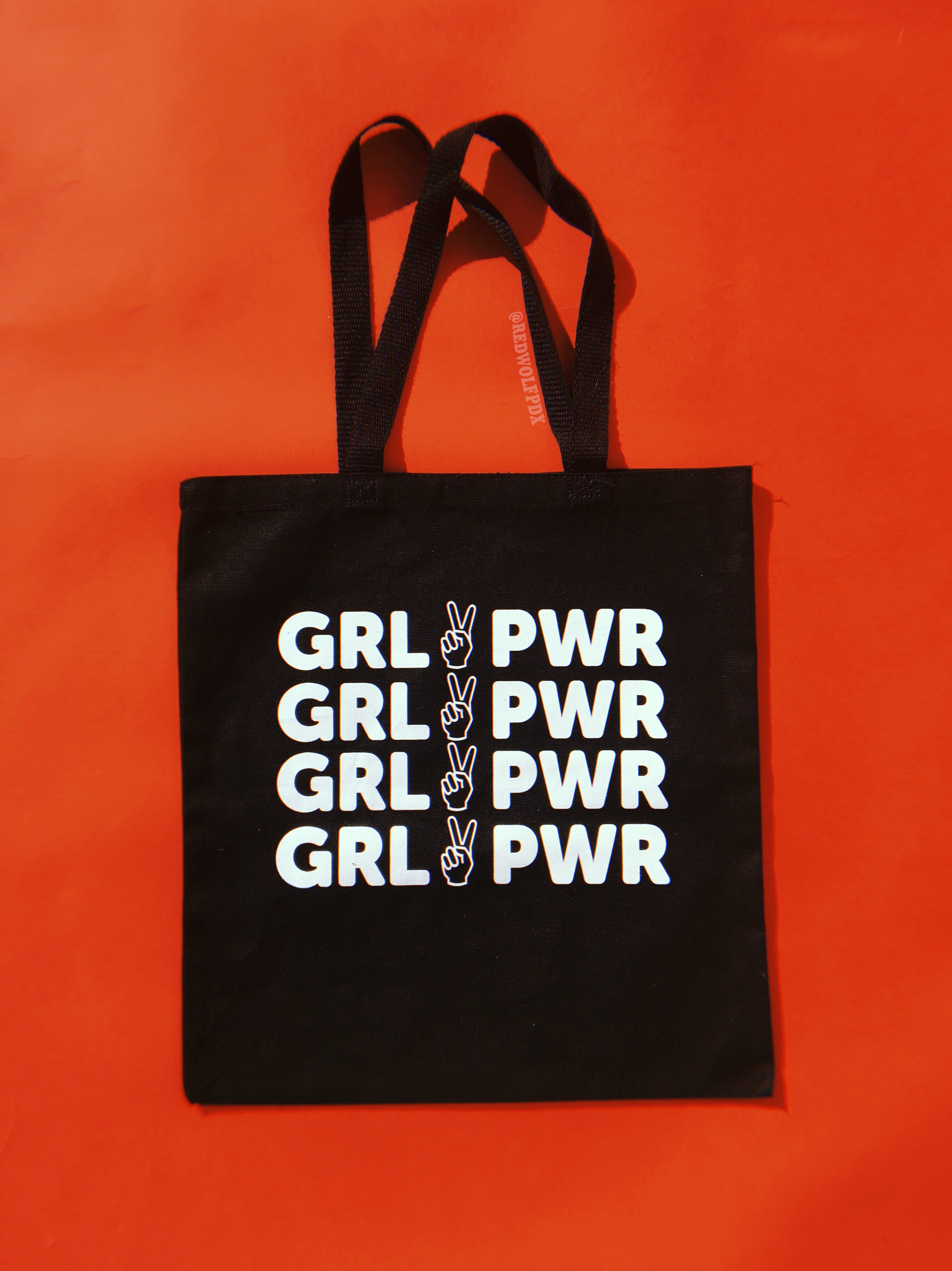 Black canvas tote bag with text 'GRL PWR' in white ink screen printed across on a vintage red backdrop