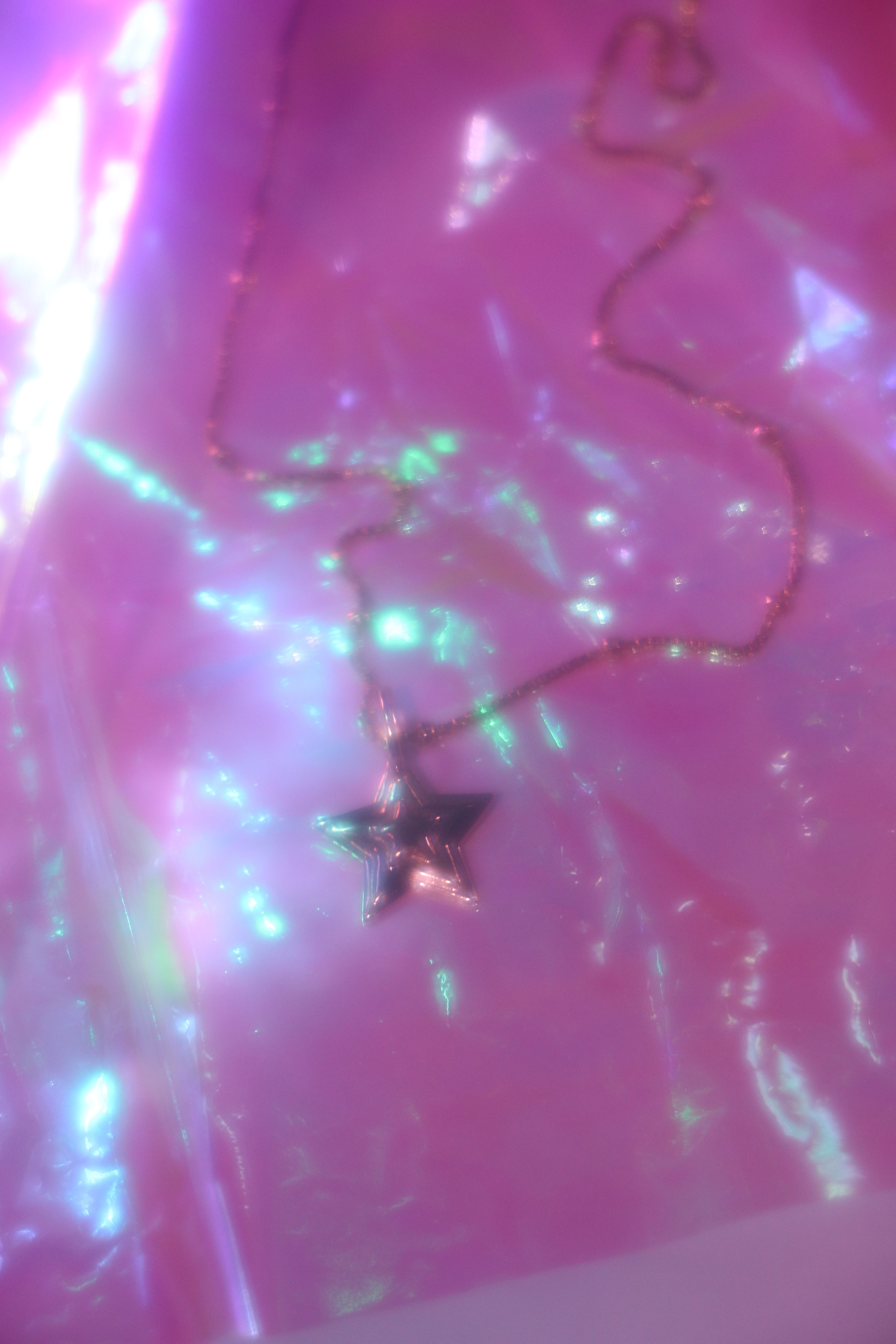 brass 3-d layered starburst charm hanging on a brass chain on shiny pink backbround