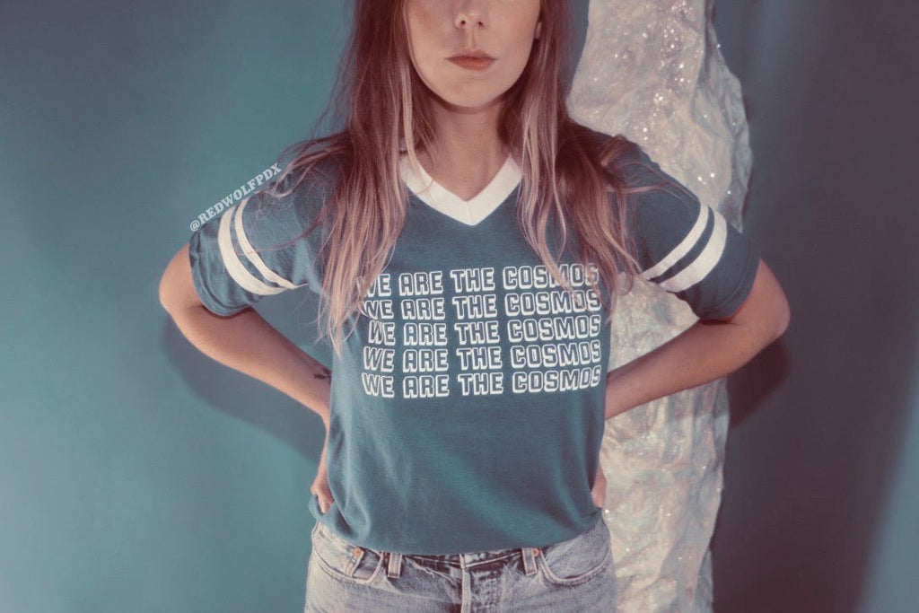 Blue t-shirt with 'We Are The Cosmos' text being worn with a blue backdrop