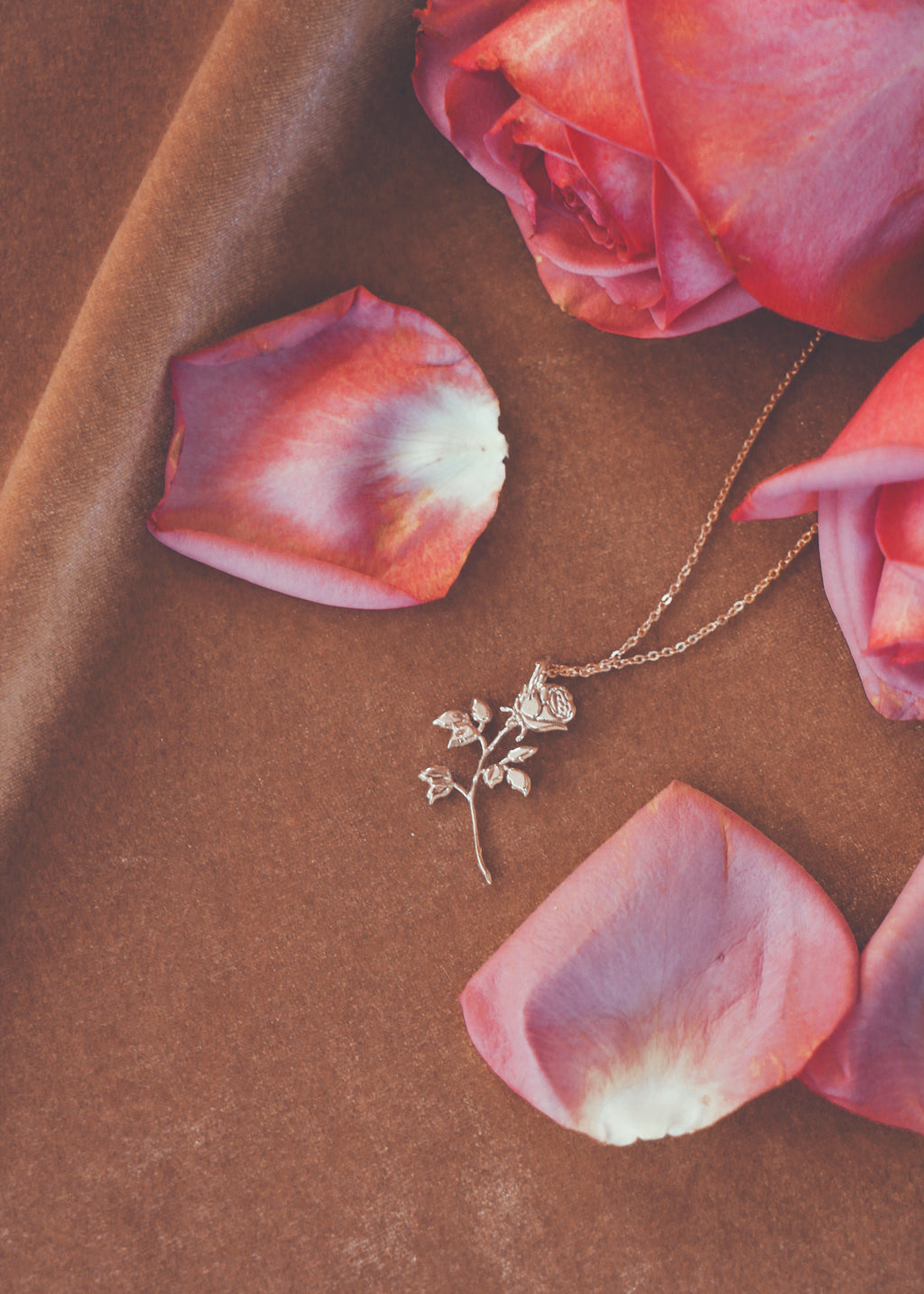 brass rose charm on brass chain on gold velvet background with pink rose petals scattered around