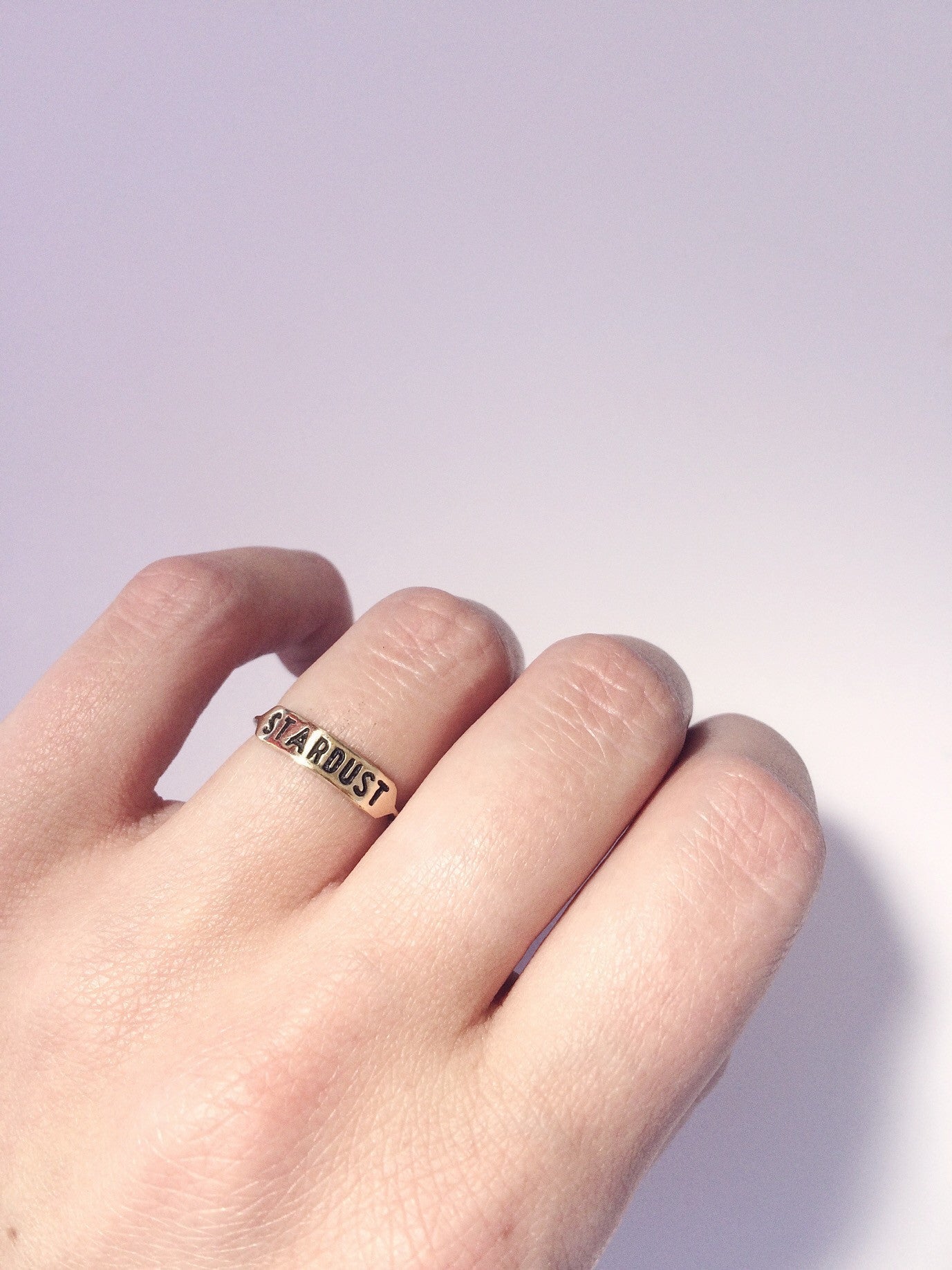 a brass ring with text 'STARDUST' engraved across it being worn on a hand against a white background