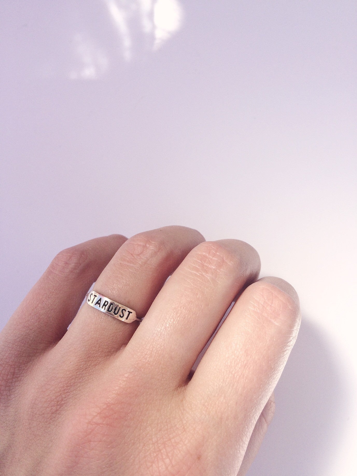 sterling silver ring with text 'STARDUST' engraved across it being worn on a hand against a white background