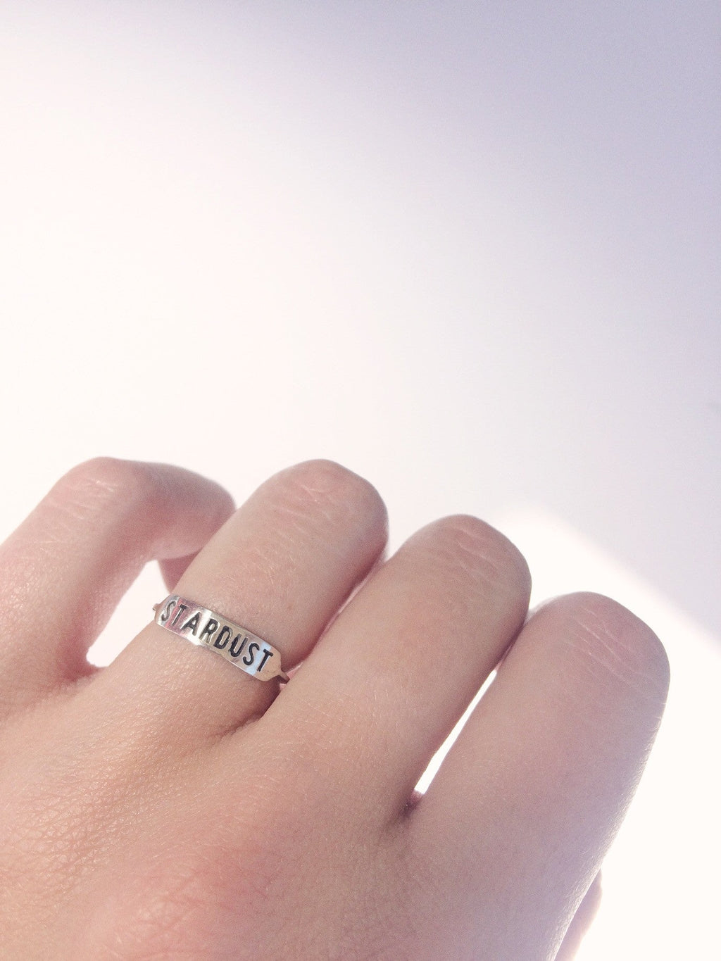 a sterling silver ring with text 'STARDUST' engraved across it being worn on a hand against a white background
