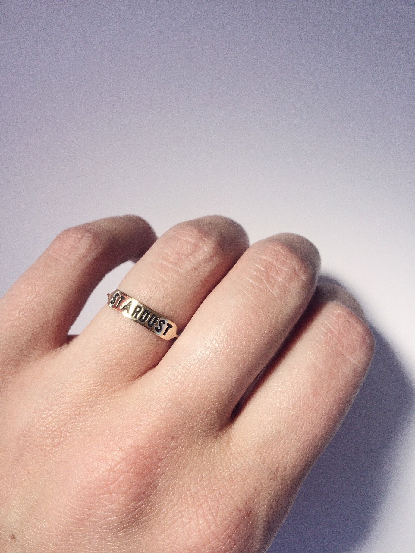 a brass ring with text 'STARDUST' engraved across it being worn on hand against a white background