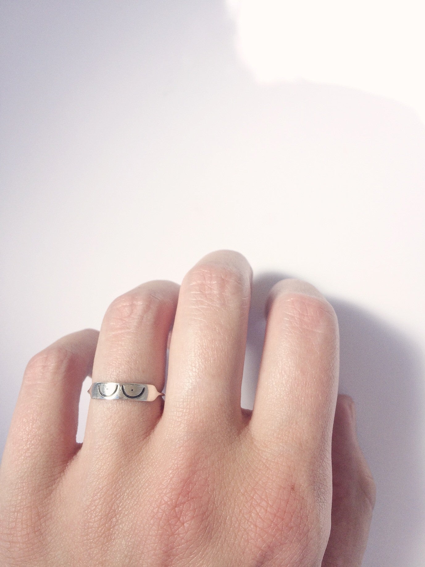 a sterling silver ring with boob illustration etched into it being worn against a white backdrop