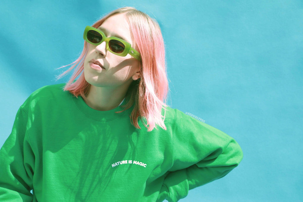 Green crewneck with text 'NATURE IS MAGIC' on corner chest being worn against blue backdrop