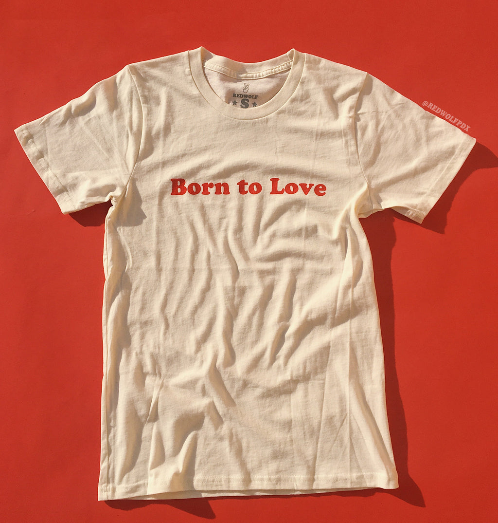 


A white crew neck t-shirt with the red graphic 'Born to Love' printed across the front, displayed on a red background.