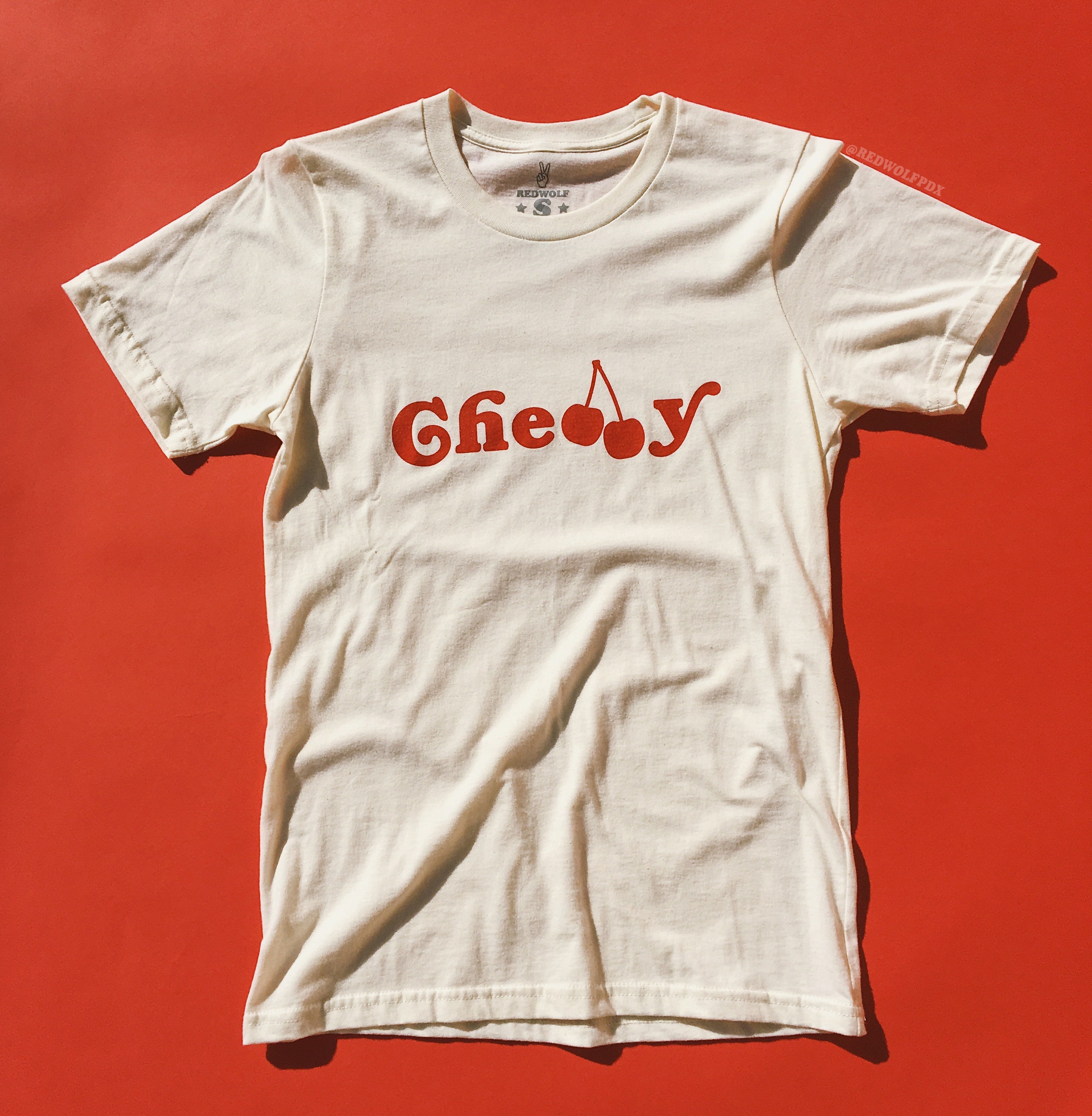 beige white graphic tee with text 'Cherry' screen printed across in red ink on a vintage red background