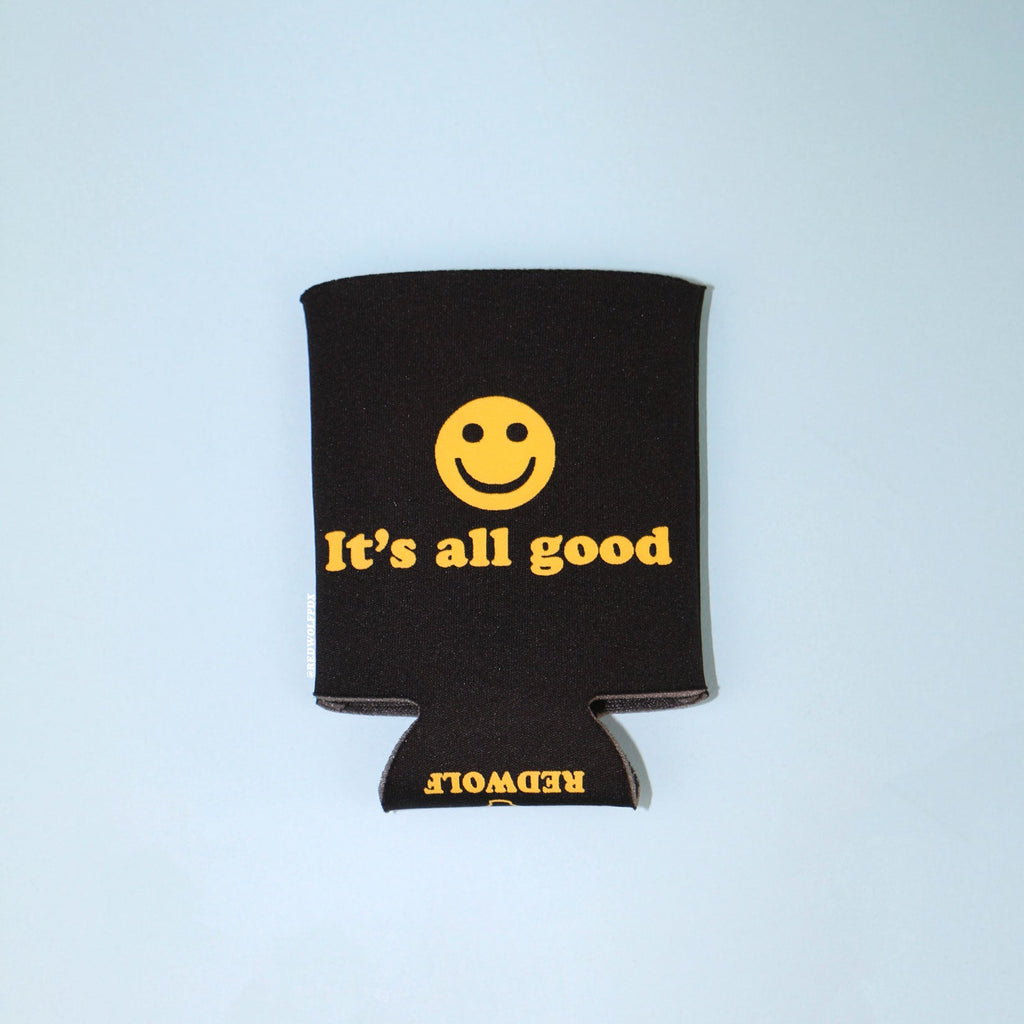 black neoprene drink sleeve with text 'It's all good' with smiley face graphic in yellow ink screen printed across it. Against a light blue background.