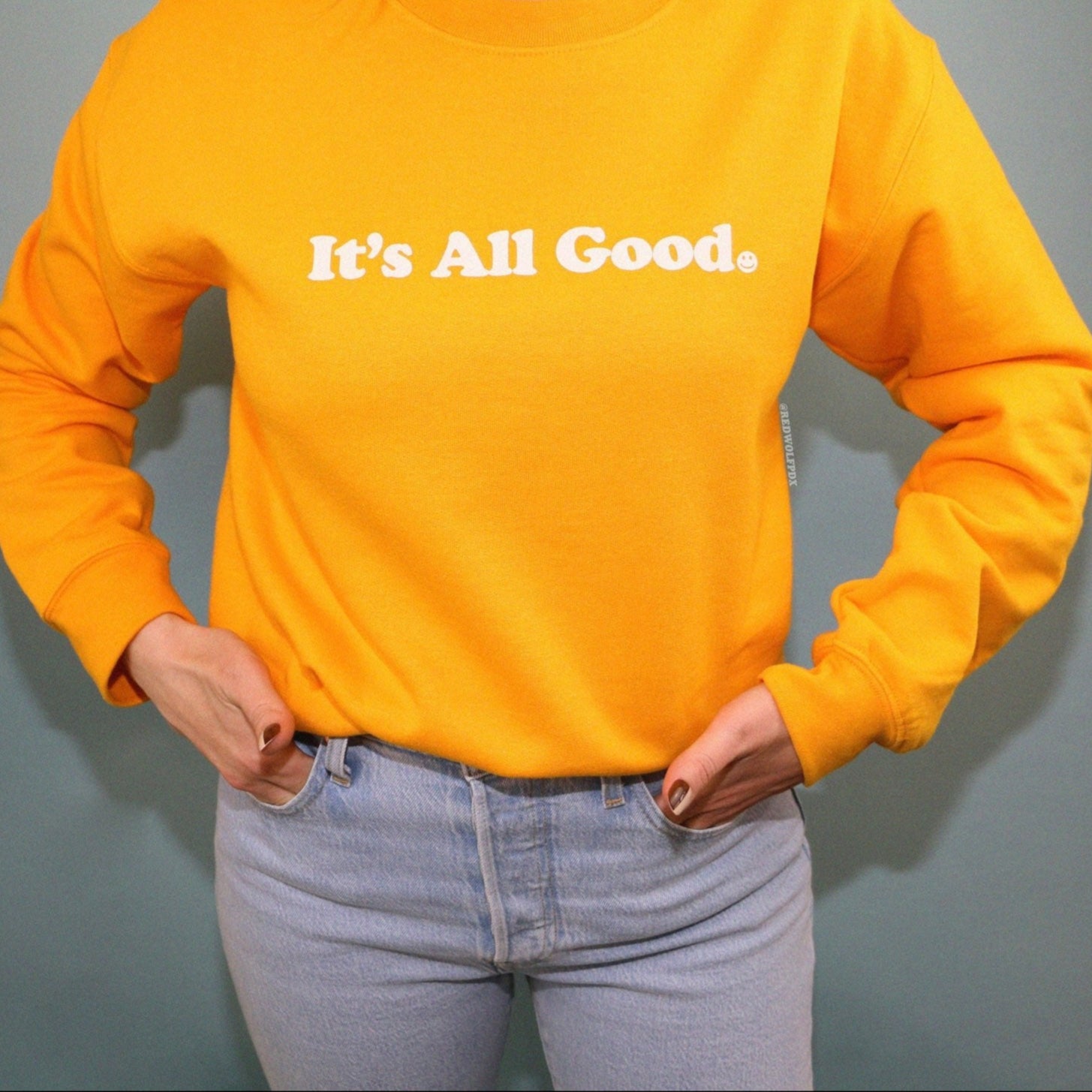 yellow crewneck sweatshirt with text 'It's All Good' being worn against blue backdrop