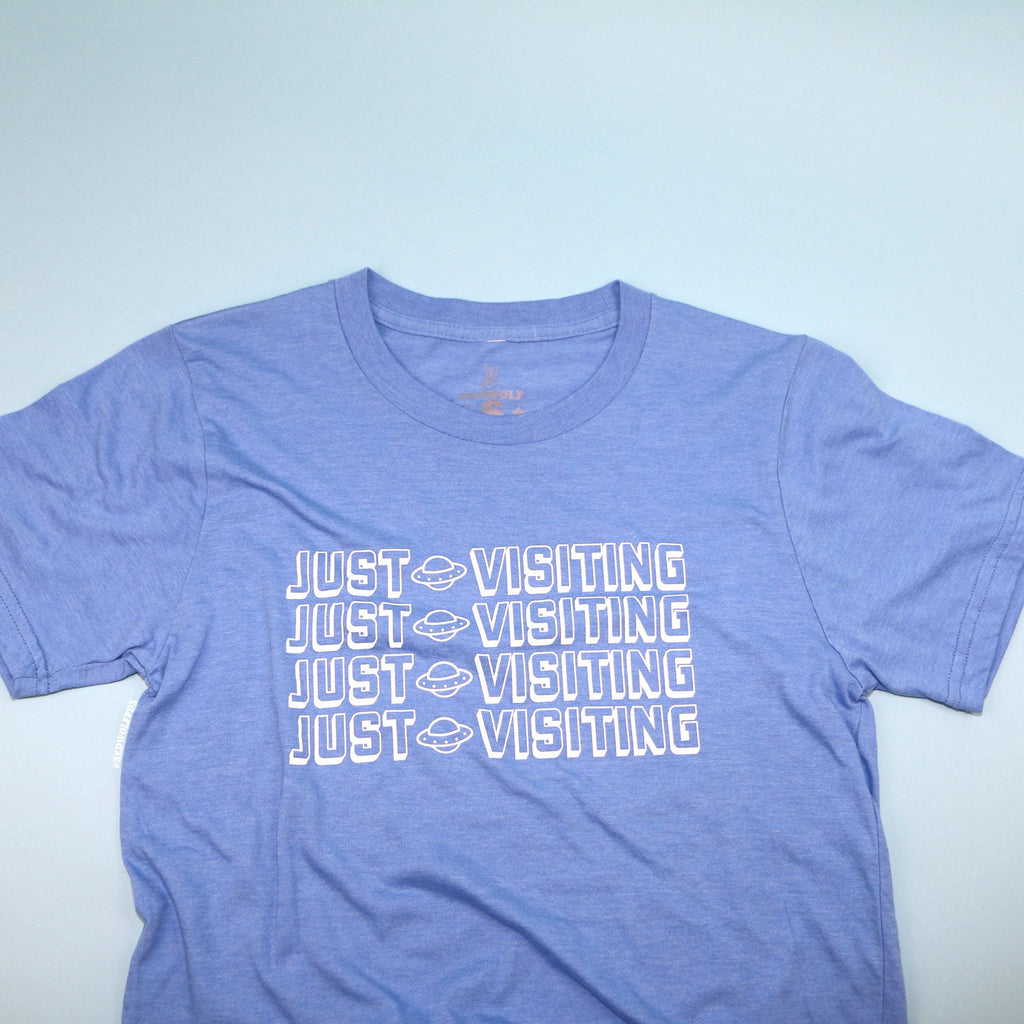 baby blue graphic tee with text 'JUST VISITING' in white ink screen printed down the front on a light blue background
