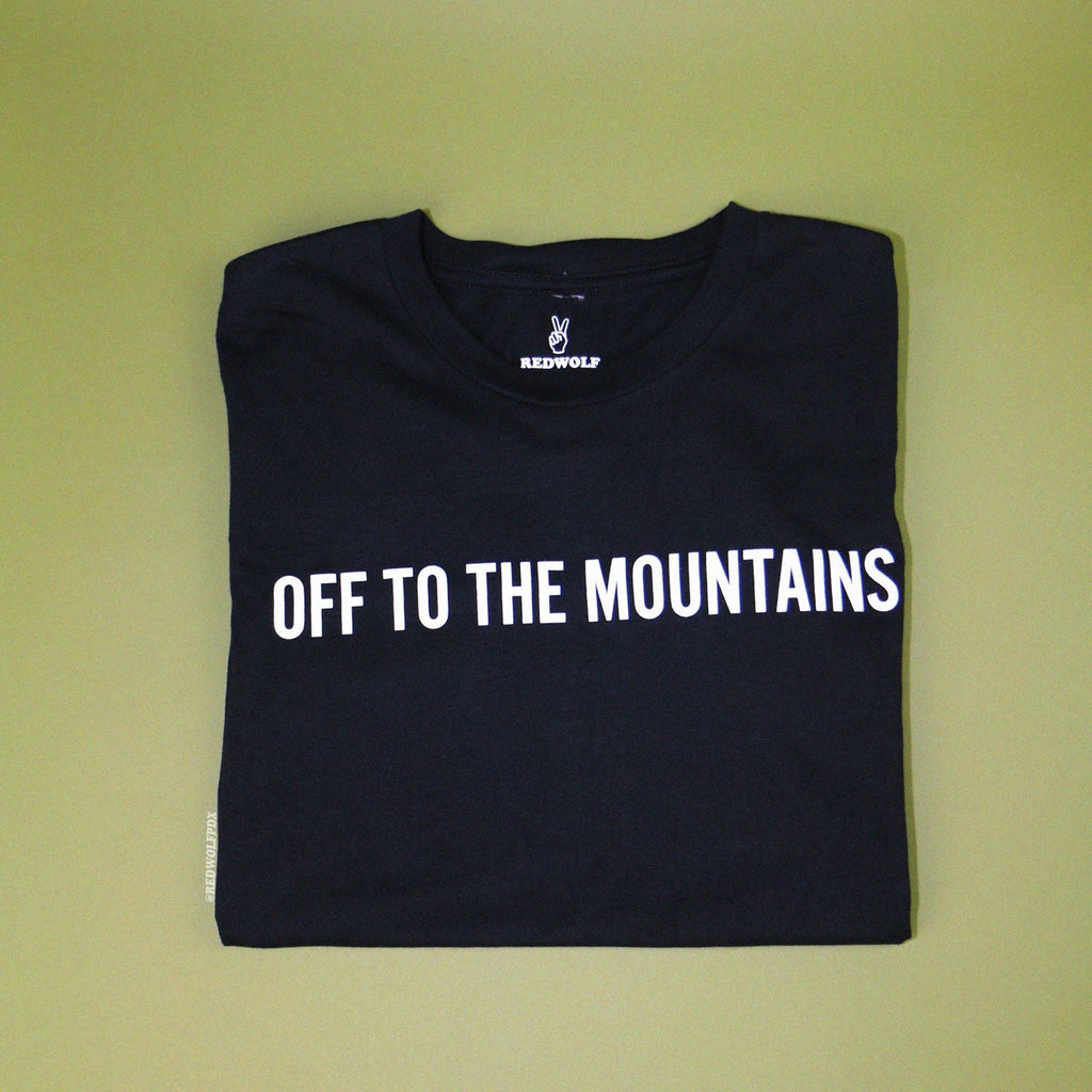 off to the mountains graphic tee folded on green backdrop