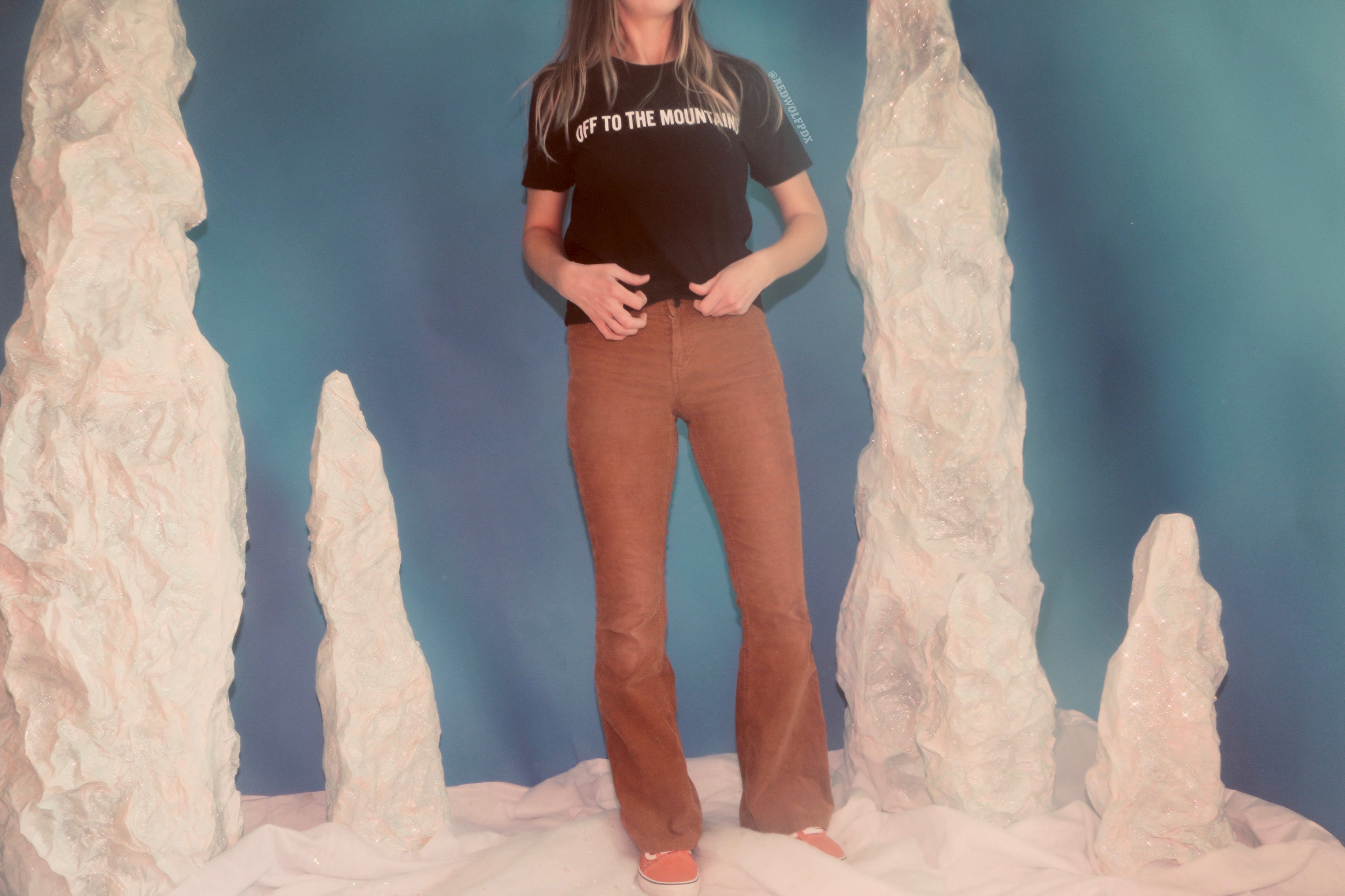 black tee with text 'OFF TO THE MOUNTAINS' screen printed across chest being worn on a winter set backdrop