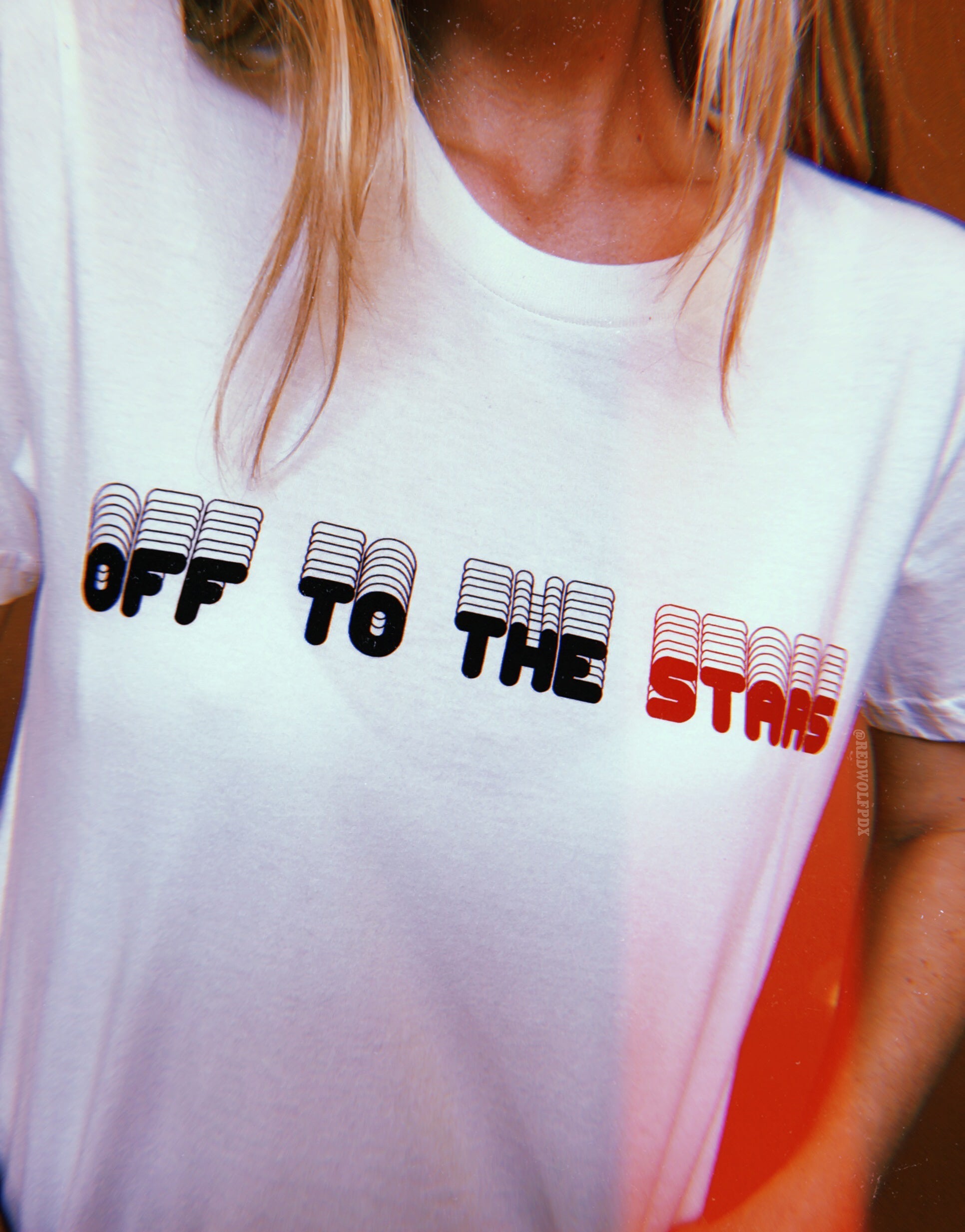 white tee with text 'OFF TO THE STARS' screen printed across the chest in black ink being worn against a brown backdrop