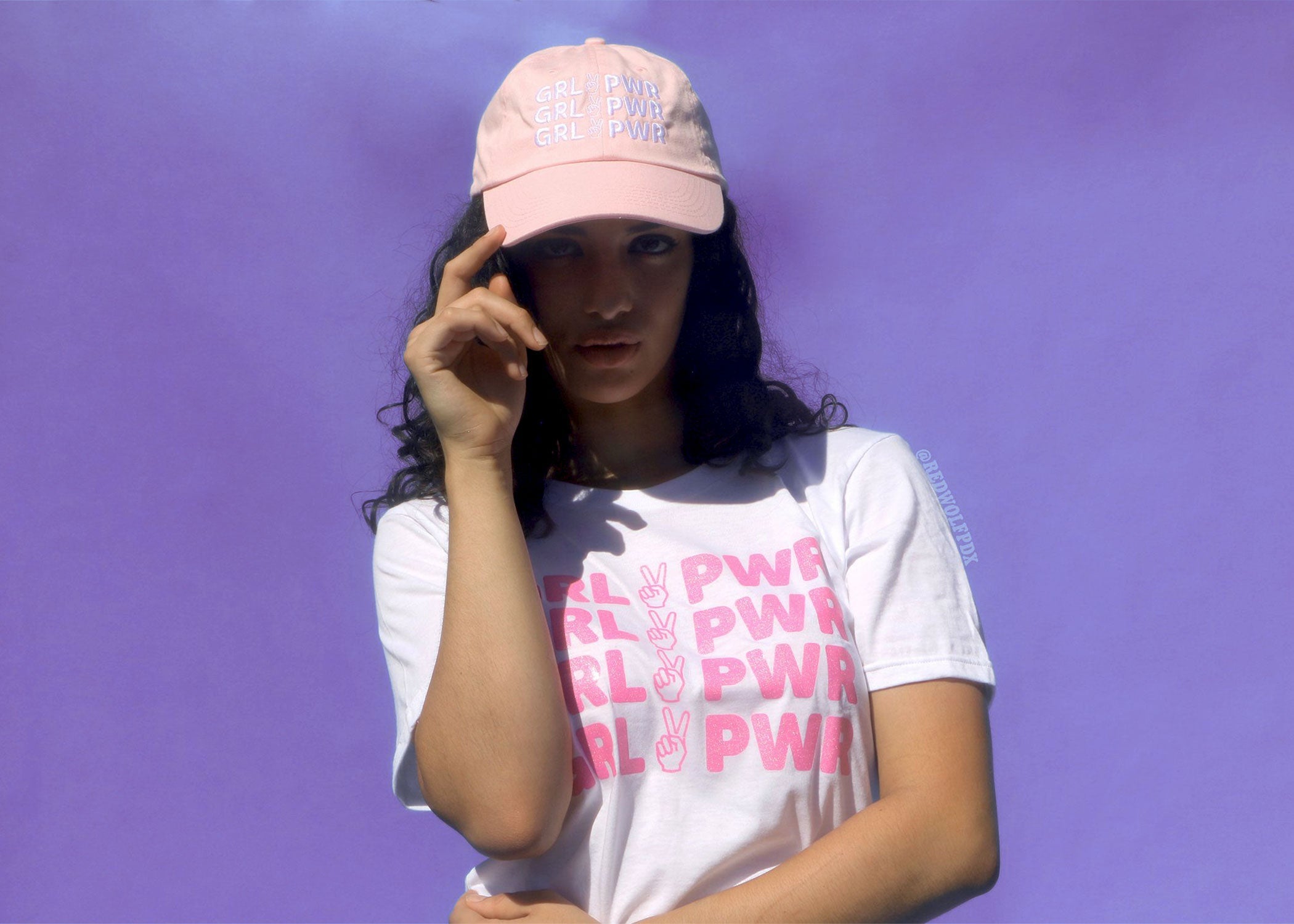 pink baseball cap with text 'GRL PWR' embroidered across being worn in front of retro purple backdrop 