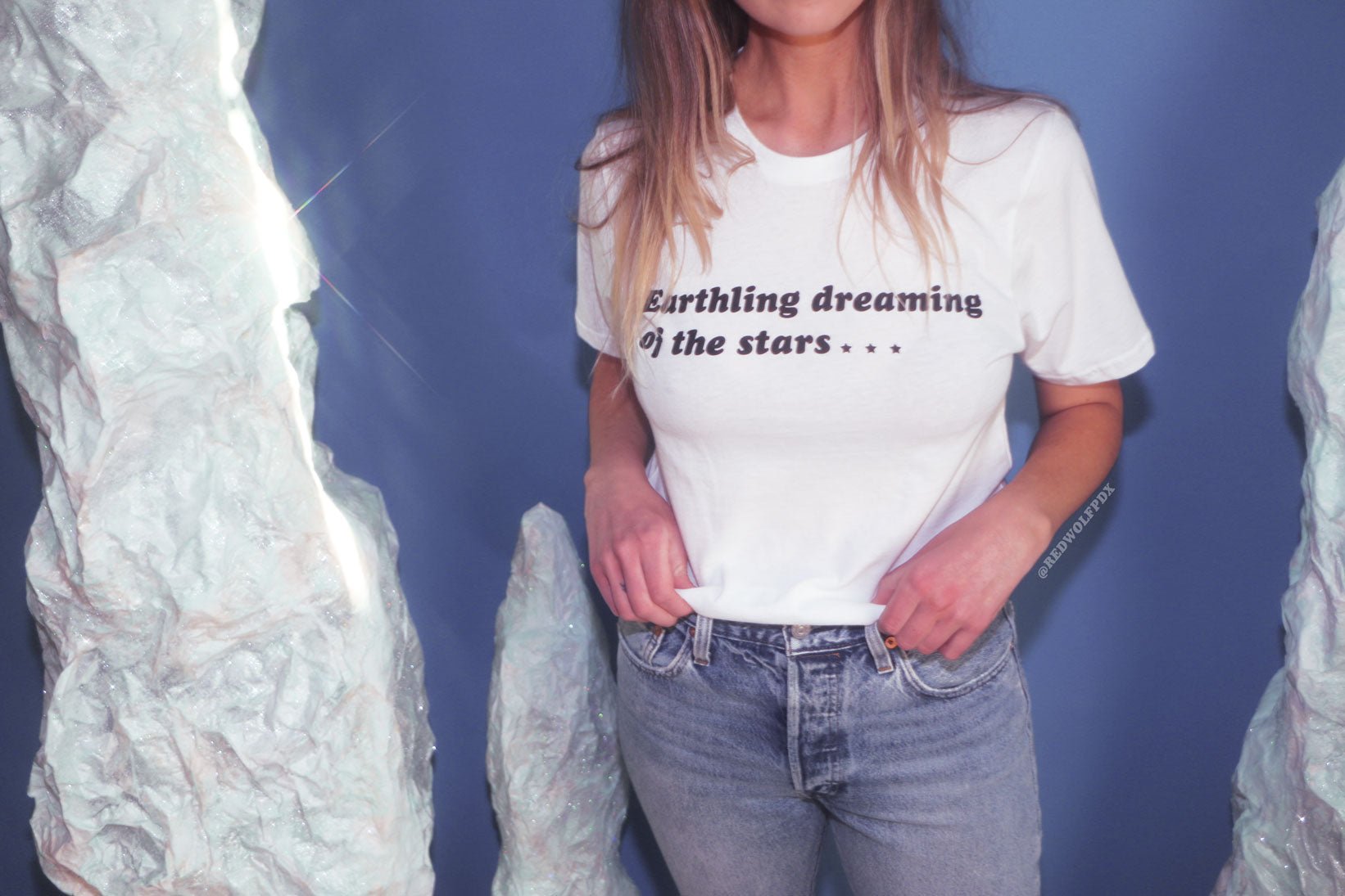 White t-shirt with text 'Earthling dreaming of the stars...' being worn in front of a space backdrop