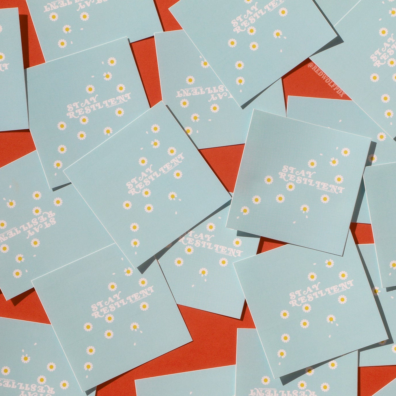 scattered baby blue square stickers with the text 'STAY RESILIENT' on them with daisy illustrations on red backdrop