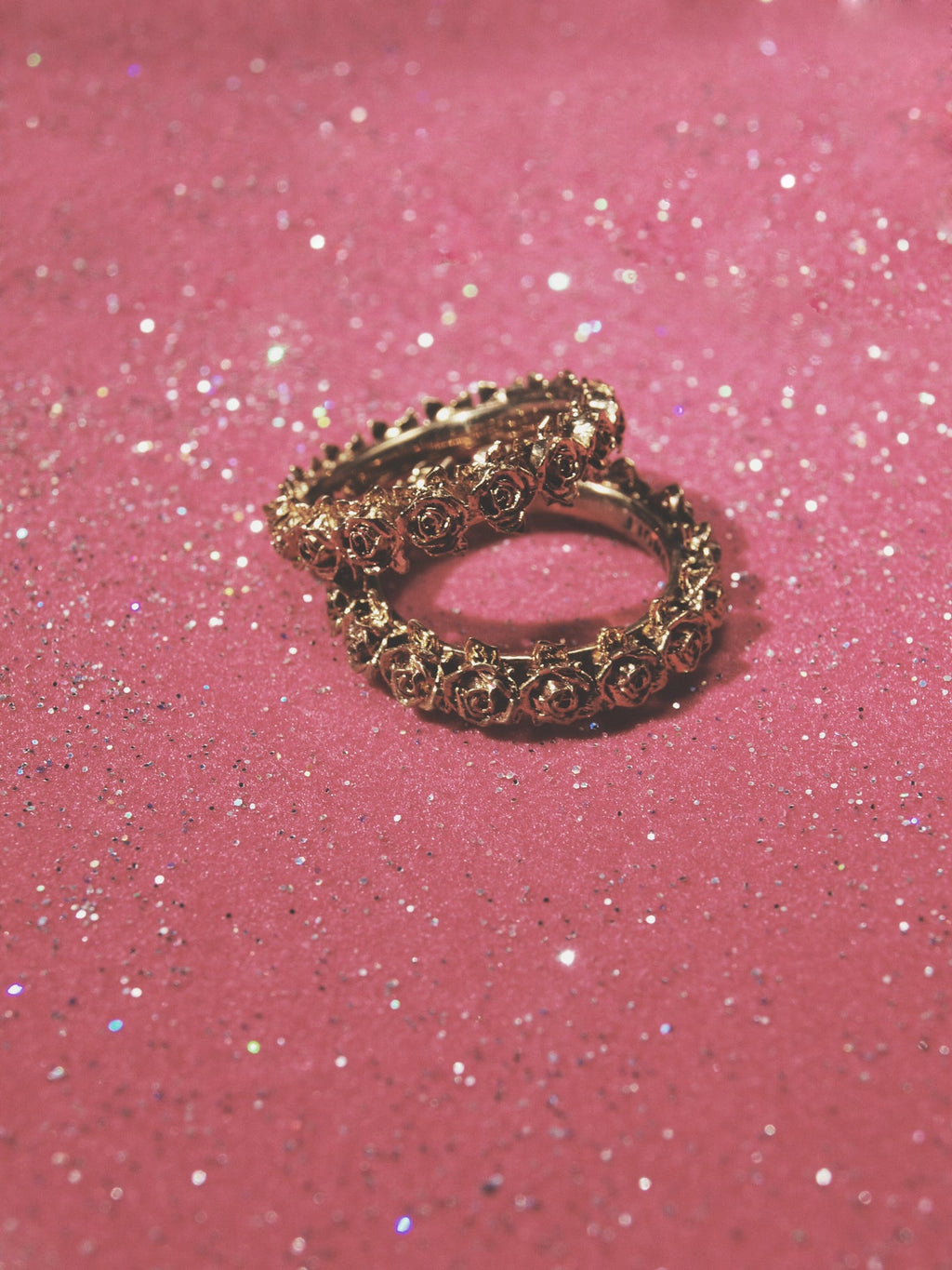 Two brass rose wreath band rings on sparkly pink backdrop