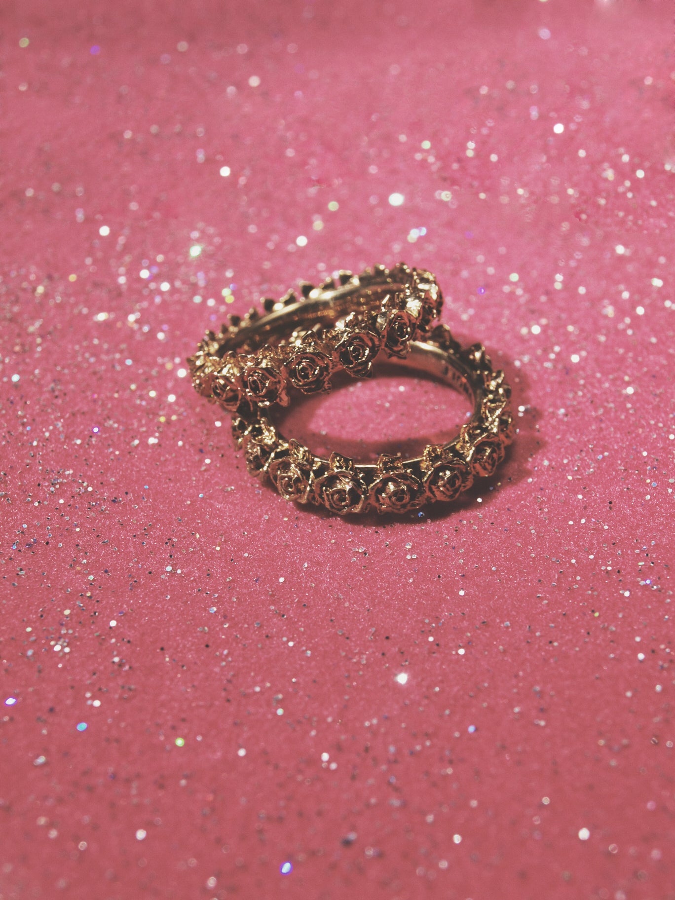 Two brass rose wreath band rings on sparkly pink backdrop