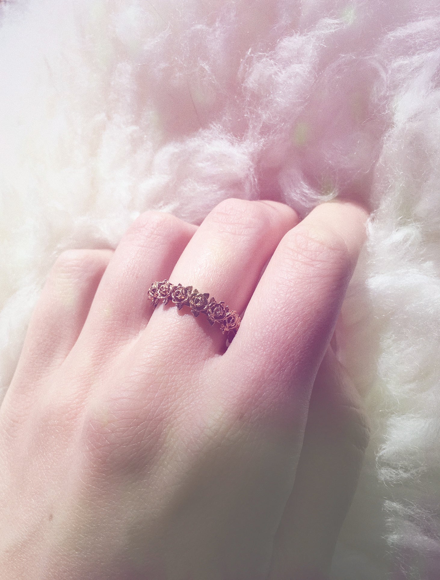 Brass rose wreath band ring being worn on hand against a white faux fur rug backdrop