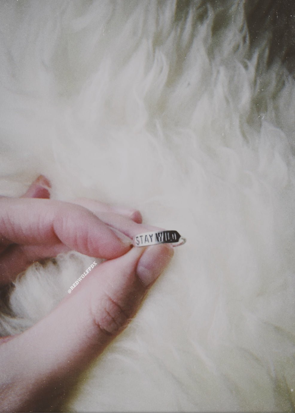 sterling silver ring with text 'STAY WILD' engraved on it being held up by hand against a faux fur rug