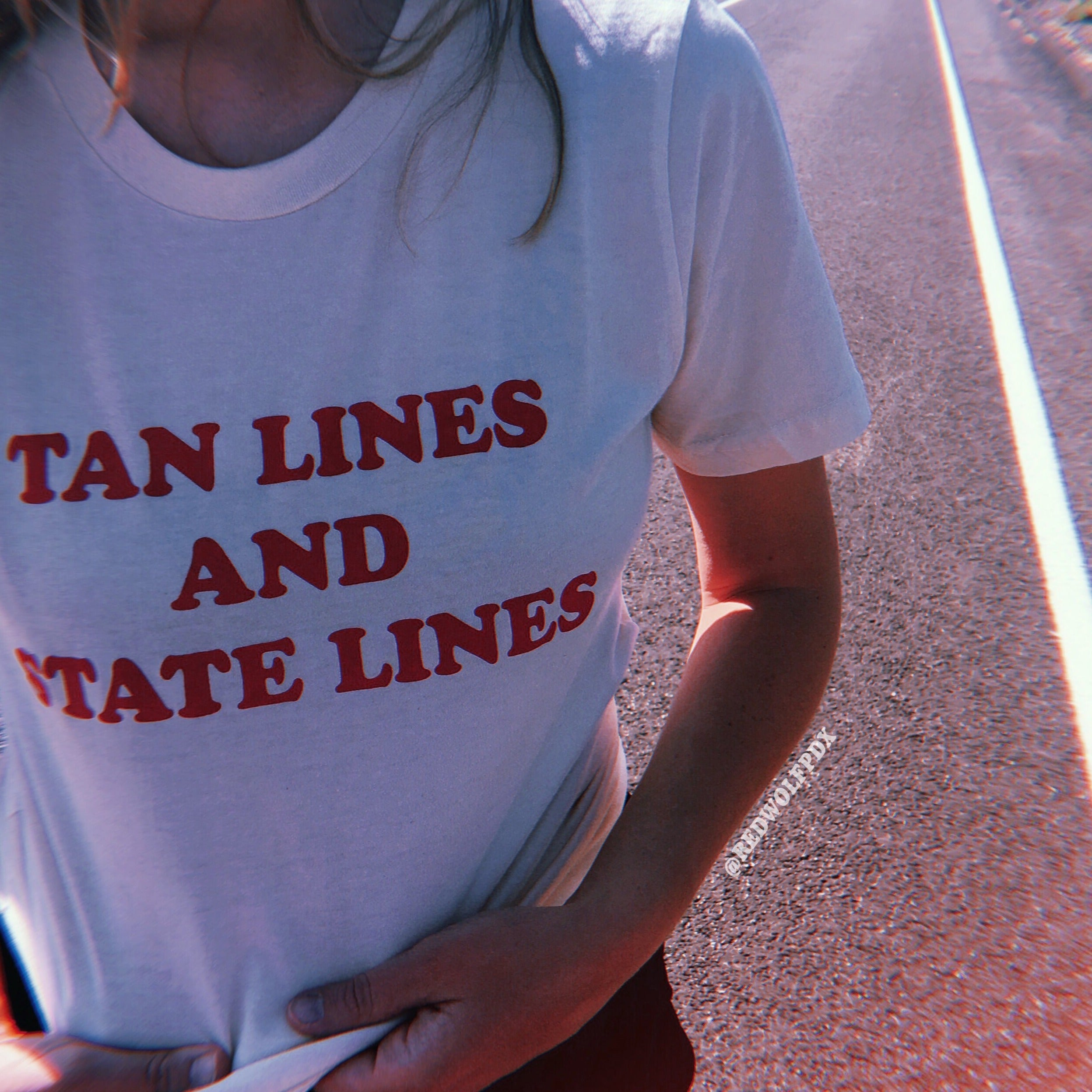 white tee with text 'TAN LINES AND STATE LINES' screen printed in red ink across chest being worn on side of road