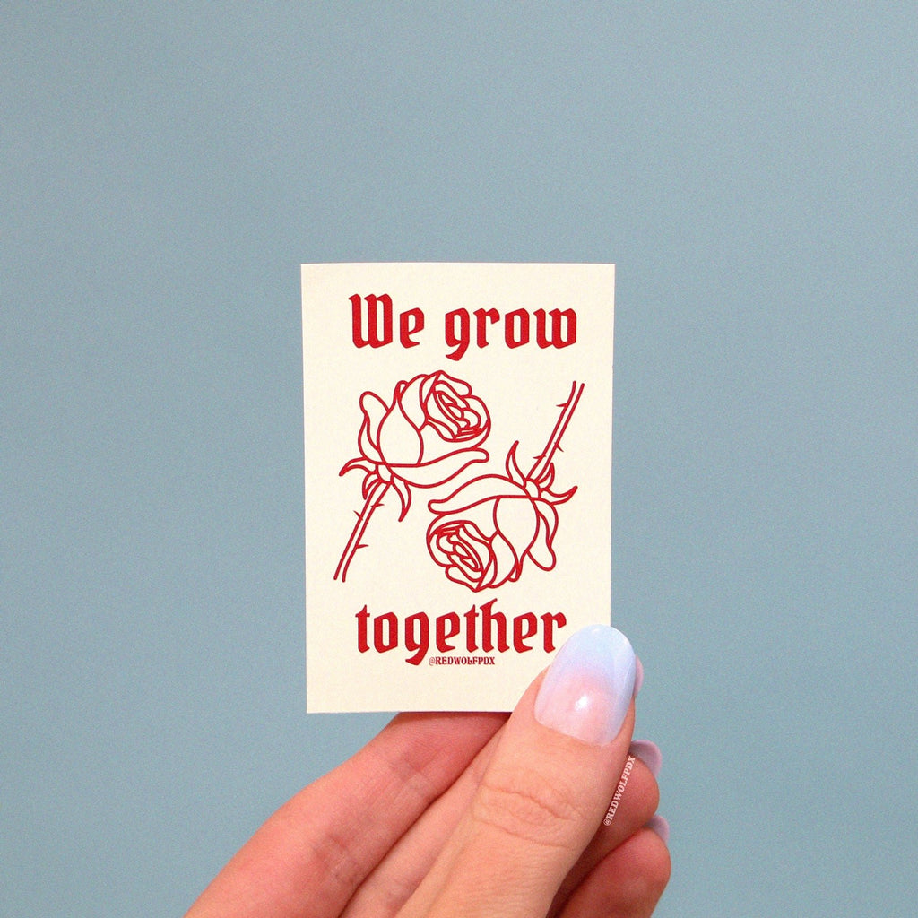 we grow together sticker with rose illustration being held up to a baby blue backdrop
