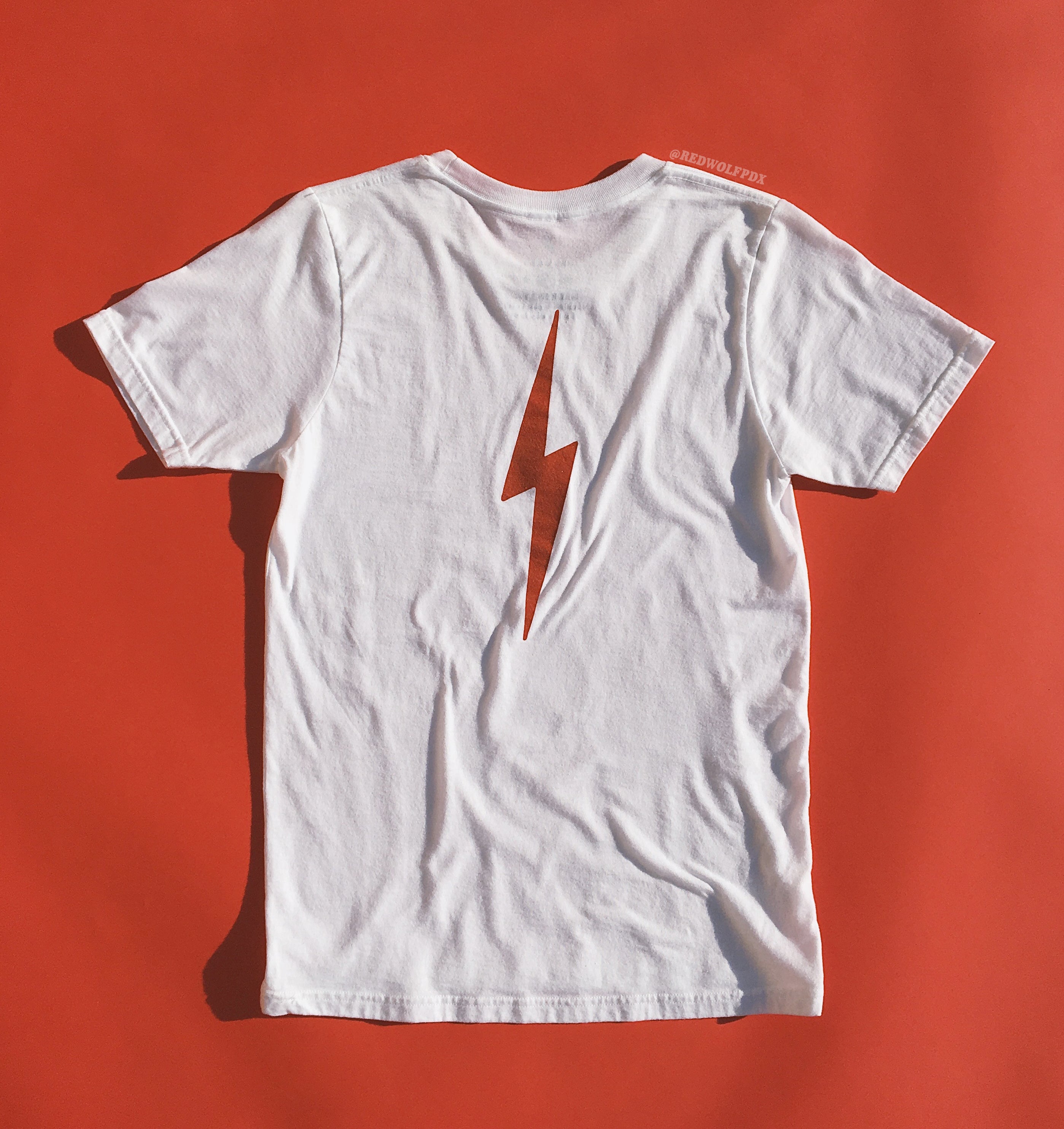 White graphic tee with lightening bolt in vintage red ink screen printed down the back of tee against a vintage red backdrop